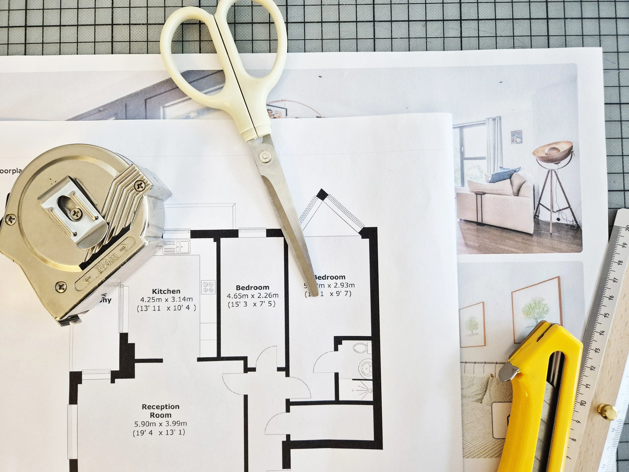 Architectural floor plan with a pair of scissors, a tape measure, and a yellow utility knife placed on top, along with interior design photos in the background.