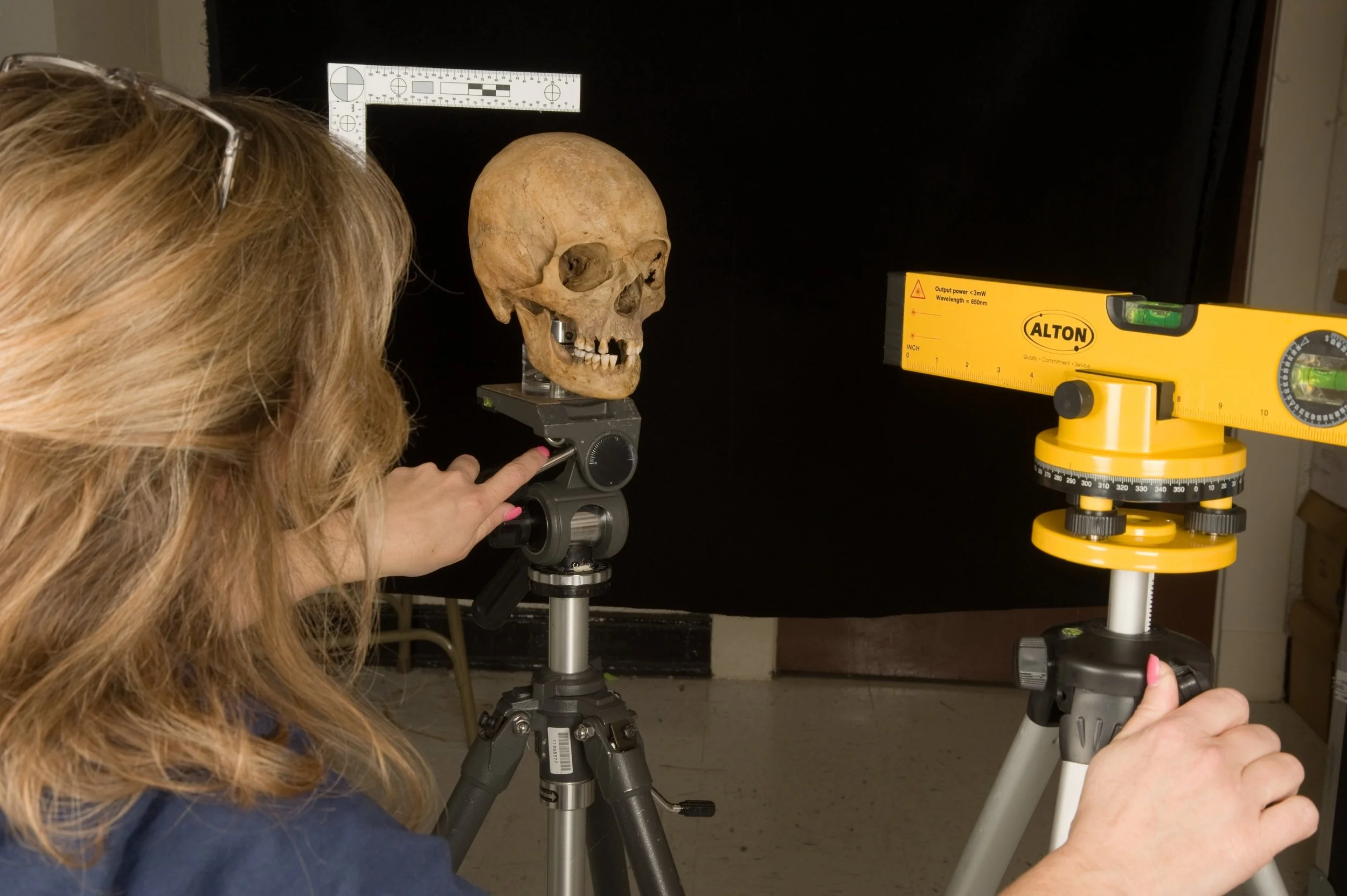 Forensic artist positioning a human skull on a tripod at the Body Farm for forensic analysis and facial reconstruction research.