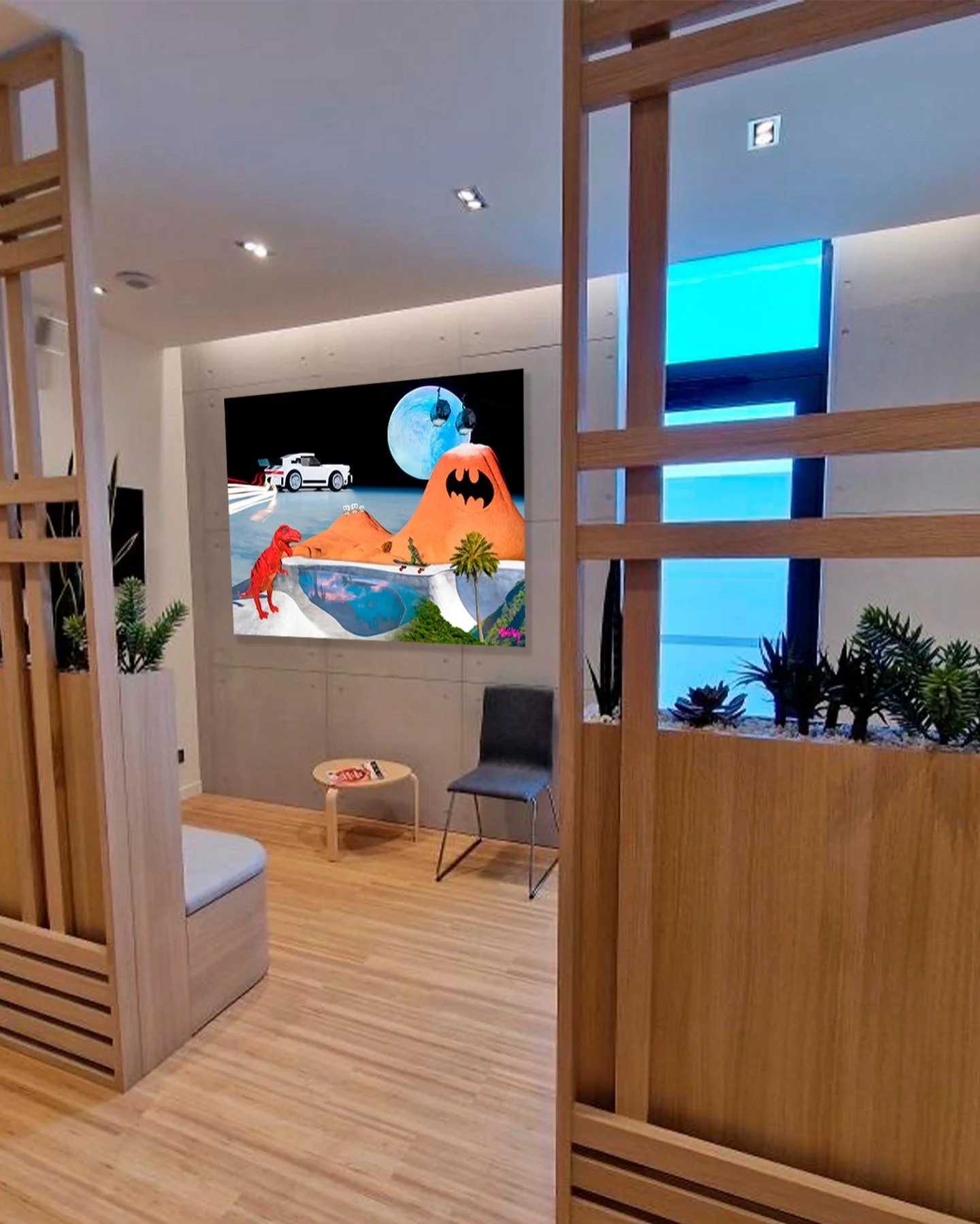 Intérieur d'une salle avec un mur vidéo montrant une image d'animation avec une montagne en forme de chauve-souris, une voiture de course, un dinosaure rouge, une cascade, un palmier et un lac, avec des plantes en pot et un siège.