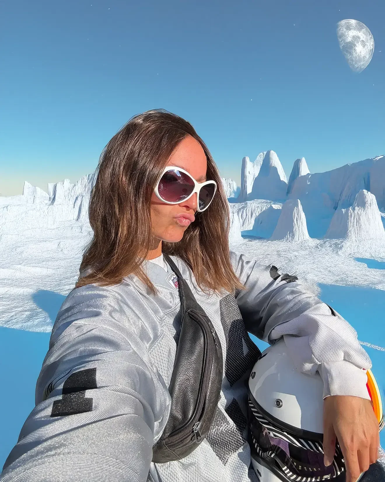 Femme portant des lunettes de soleil et un blouson d'hiver, tenant un casque de moto, dans un paysage glacé avec des icebergs, la lune visible dans le ciel.