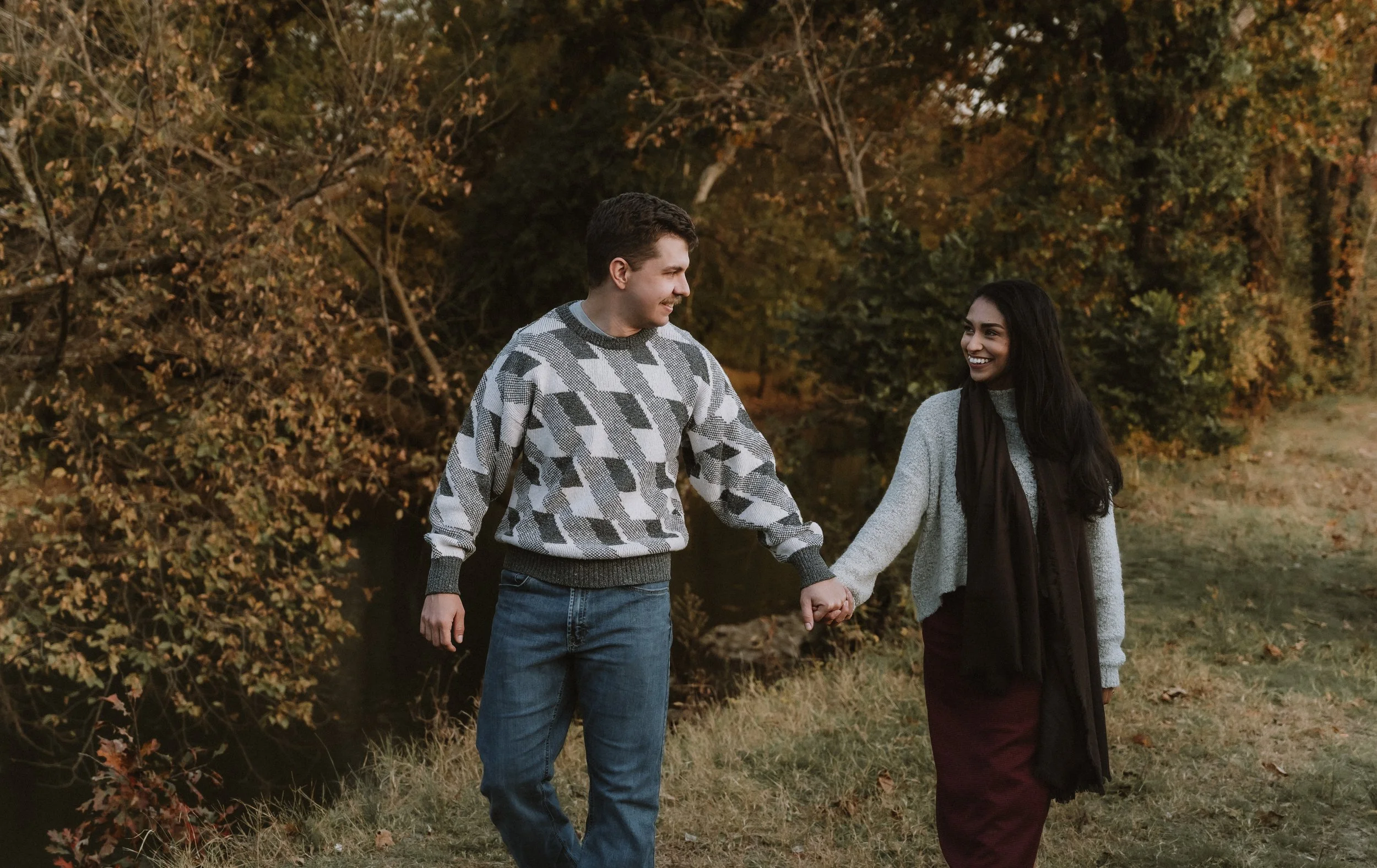 Autumn portrait of a couple walking hand in hand, surrounded by warm fall foliage and natural connection.