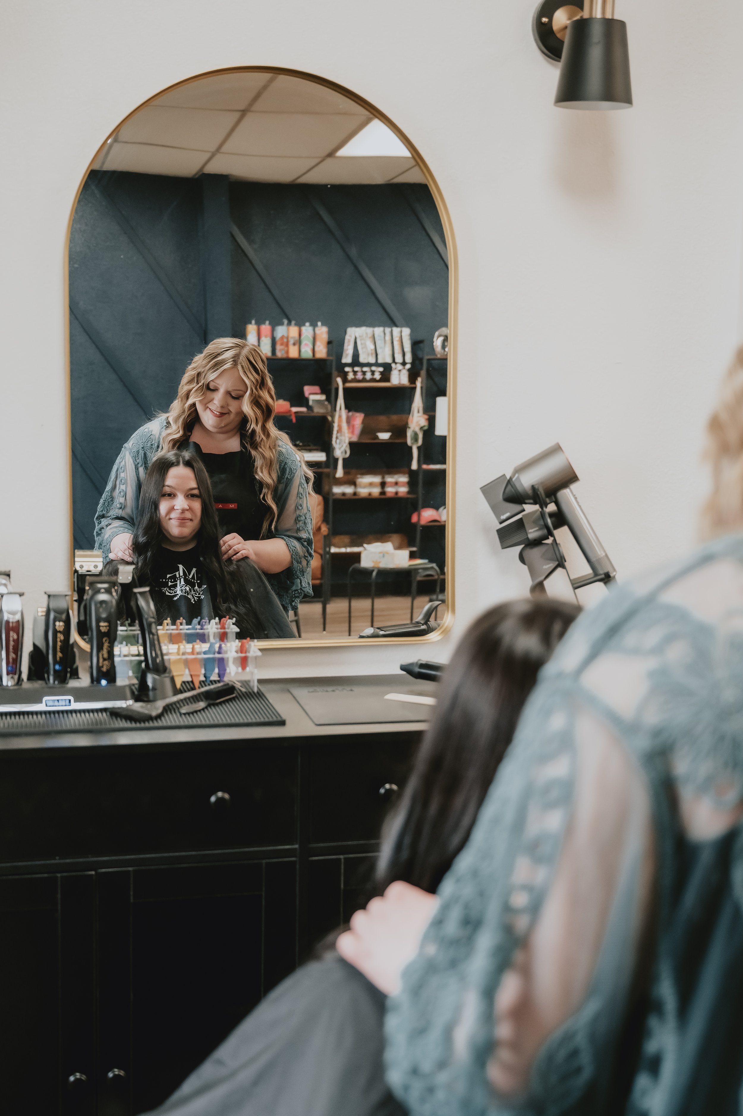 Person getting a haircut at a salon, reflected in a mirror, with hair products on the counter and shelves in the background.