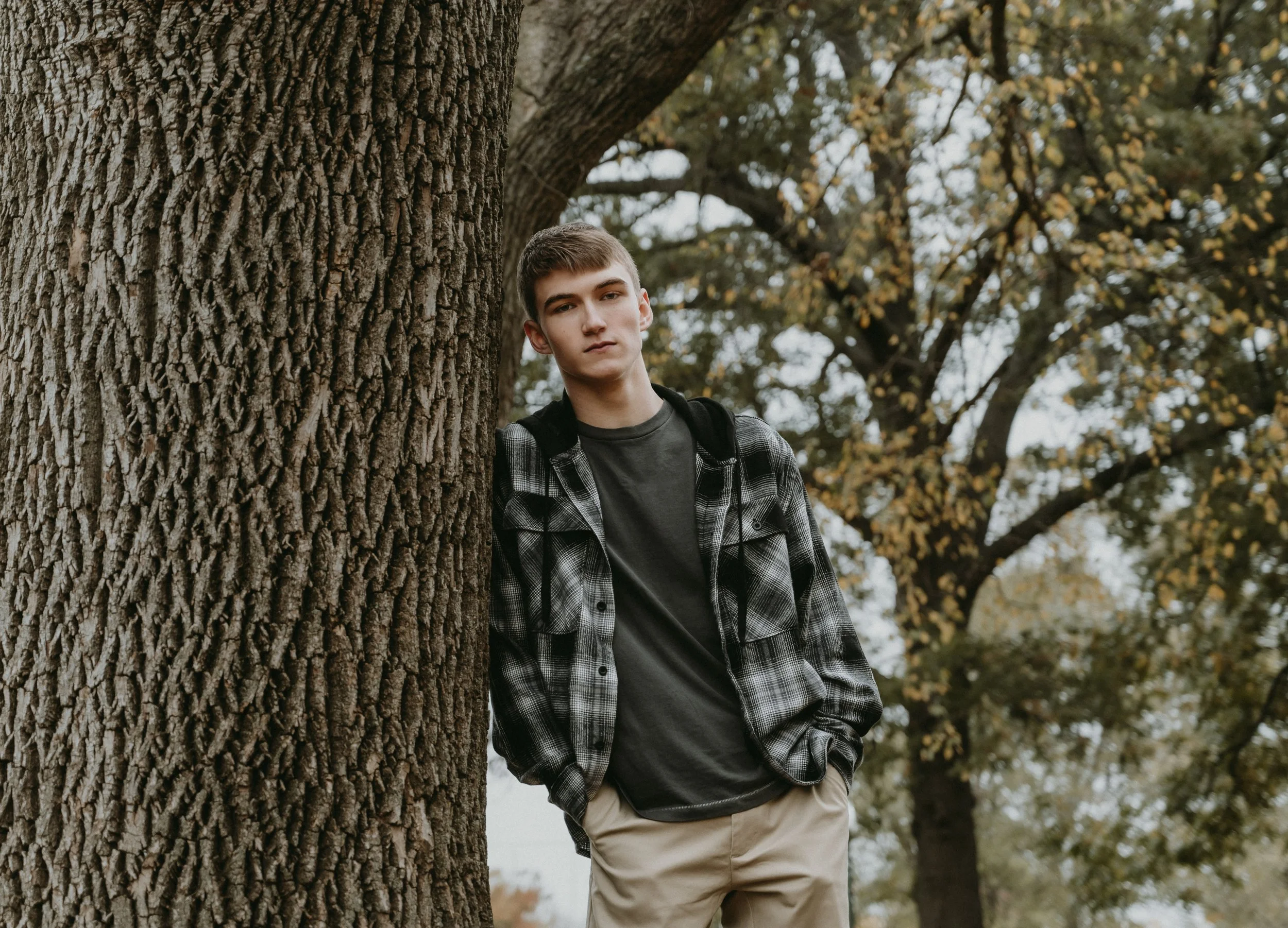 A woman with dark hair is leaning over a man with earrings and brown hair who is lying on the ground among dry grass or twigs, holding a gun in his hand.