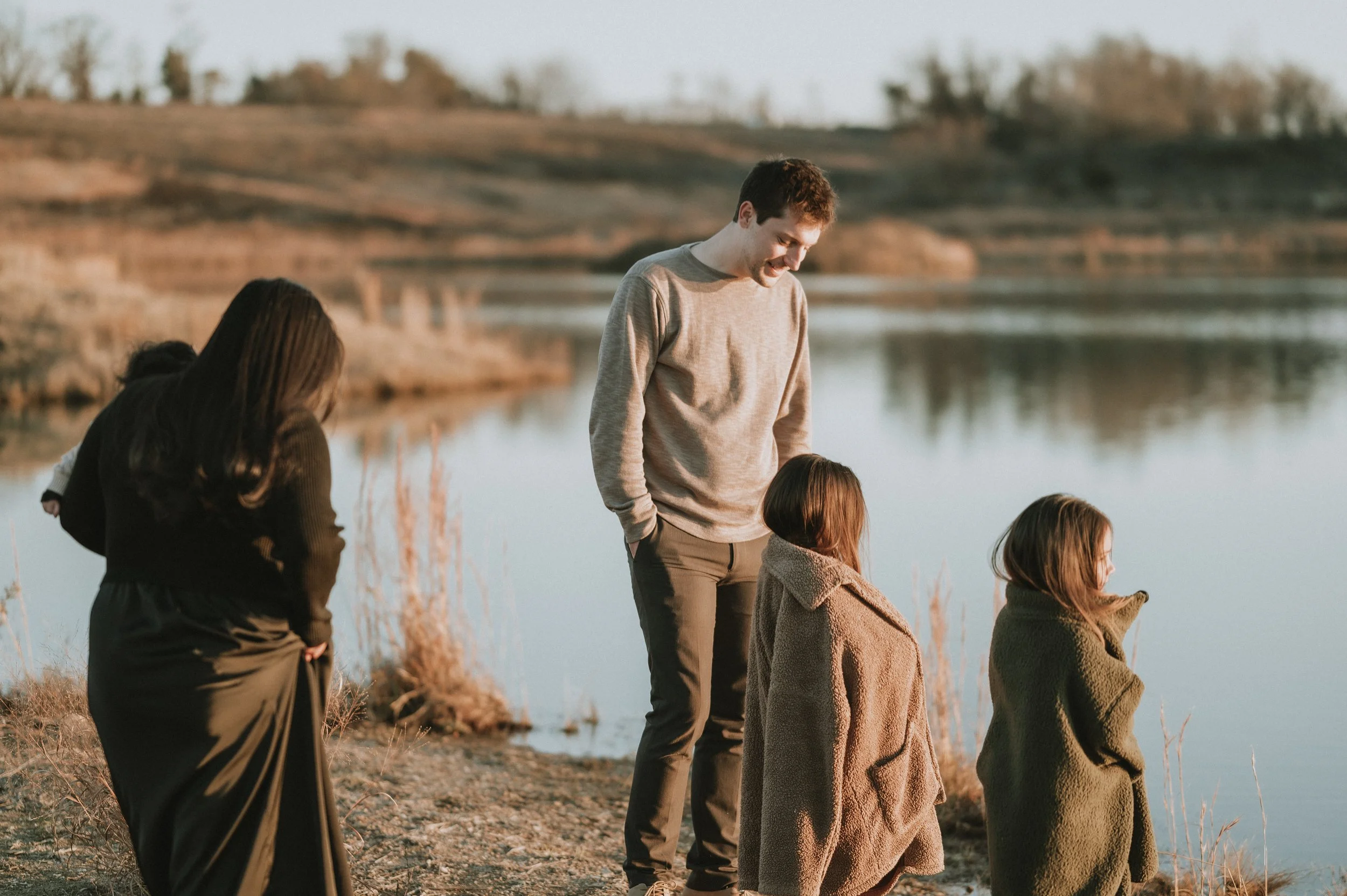 Candid family moment by a lakeside at sunset, capturing conversation, connection, and shared presence across generations.