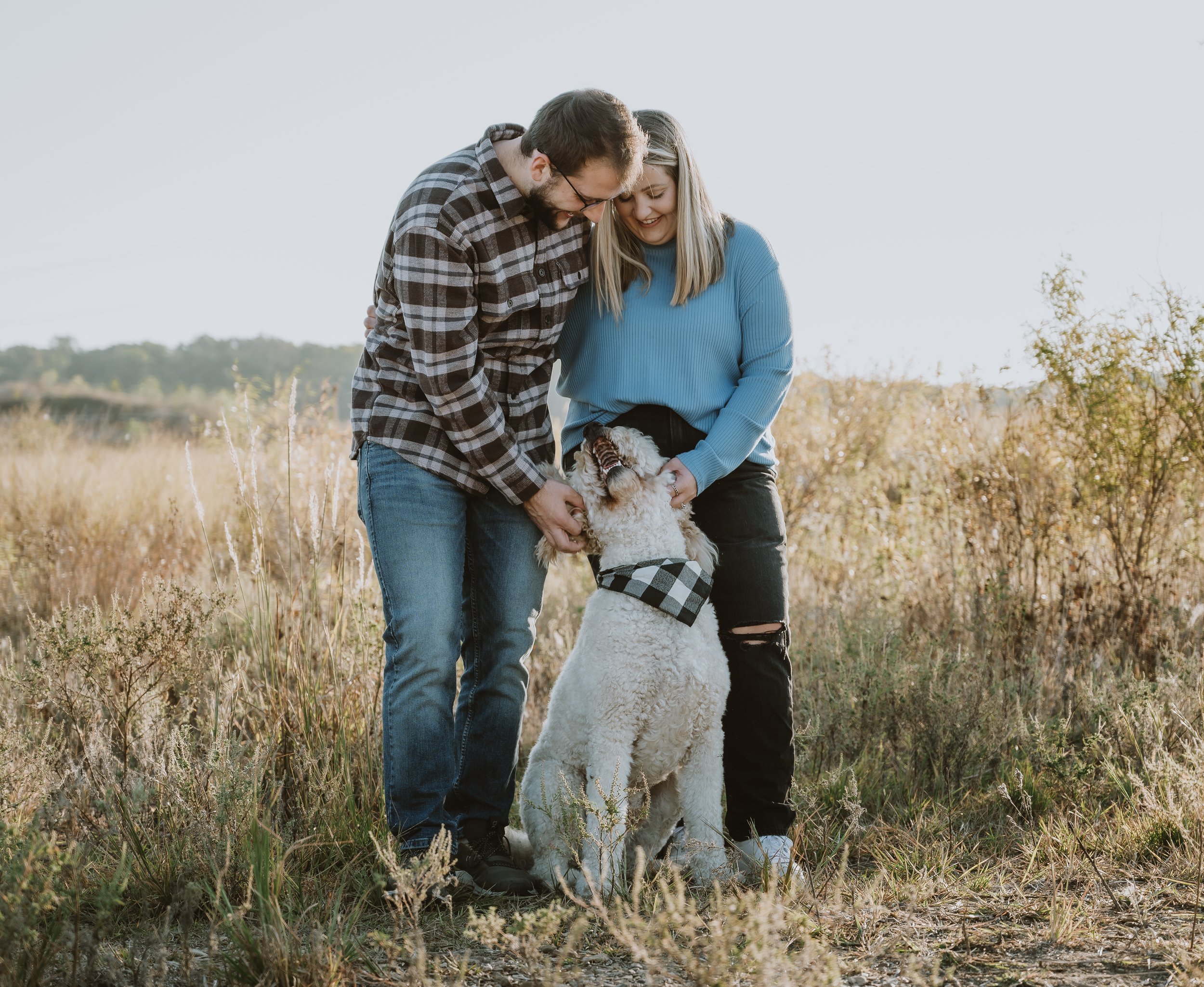 Lifestyle portrait of a couple and their dog in an open field, capturing playful connection and everyday joy.