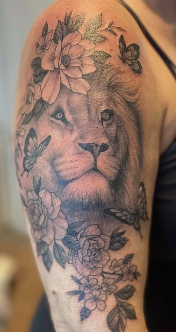 delicate lion with flowers and butterflies tattoo on upper arm