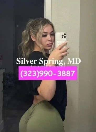 A young woman with long blonde hair taking a mirror selfie in a room with gray walls, showing part of her face and body. She is wearing a black top and olive-green pants, with text overlayed on the image reading 'Silver Spring, MD' and a phone number in pink.