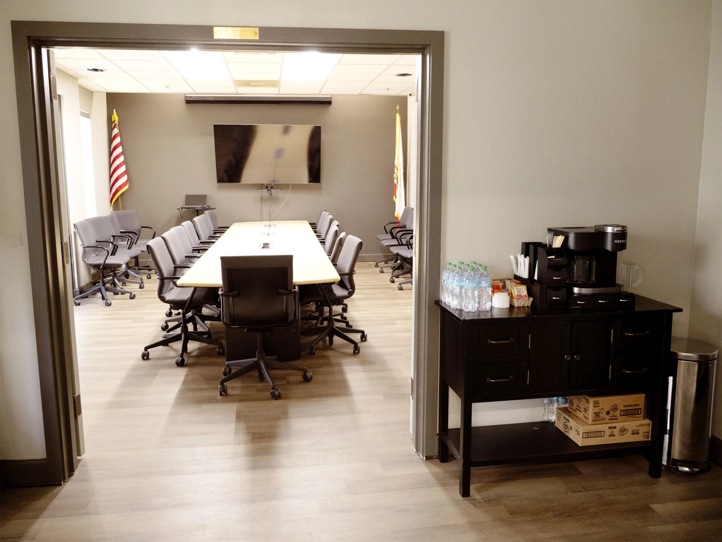 Bright image of a large conference room or board room in Benicia with 25 chairs, a table, a large screen, and a coffee station.