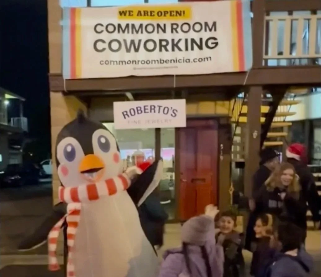 Inflatable penguin dances with children in front of a sign for Common Room Coworking