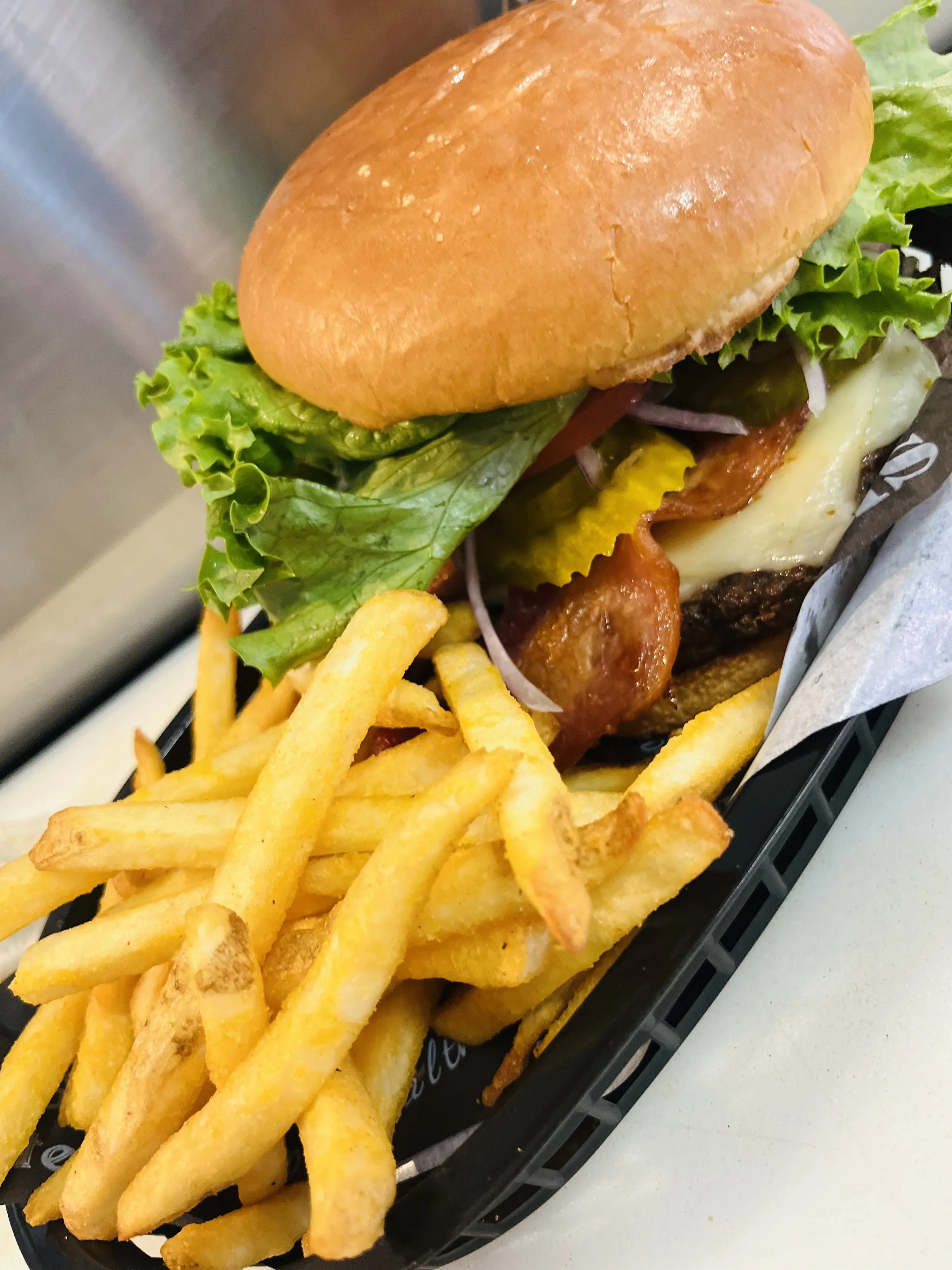 A cheeseburger with lettuce, tomato, cheese, bacon, and a bun, served with a side of French fries.