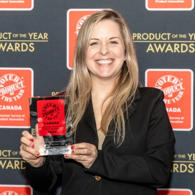 A woman with long blonde hair smiling and holding a glass award at an awards event backdrop.