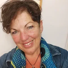 A woman with short brown hair smiling at the camera, wearing a denim jacket and a green patterned scarf.