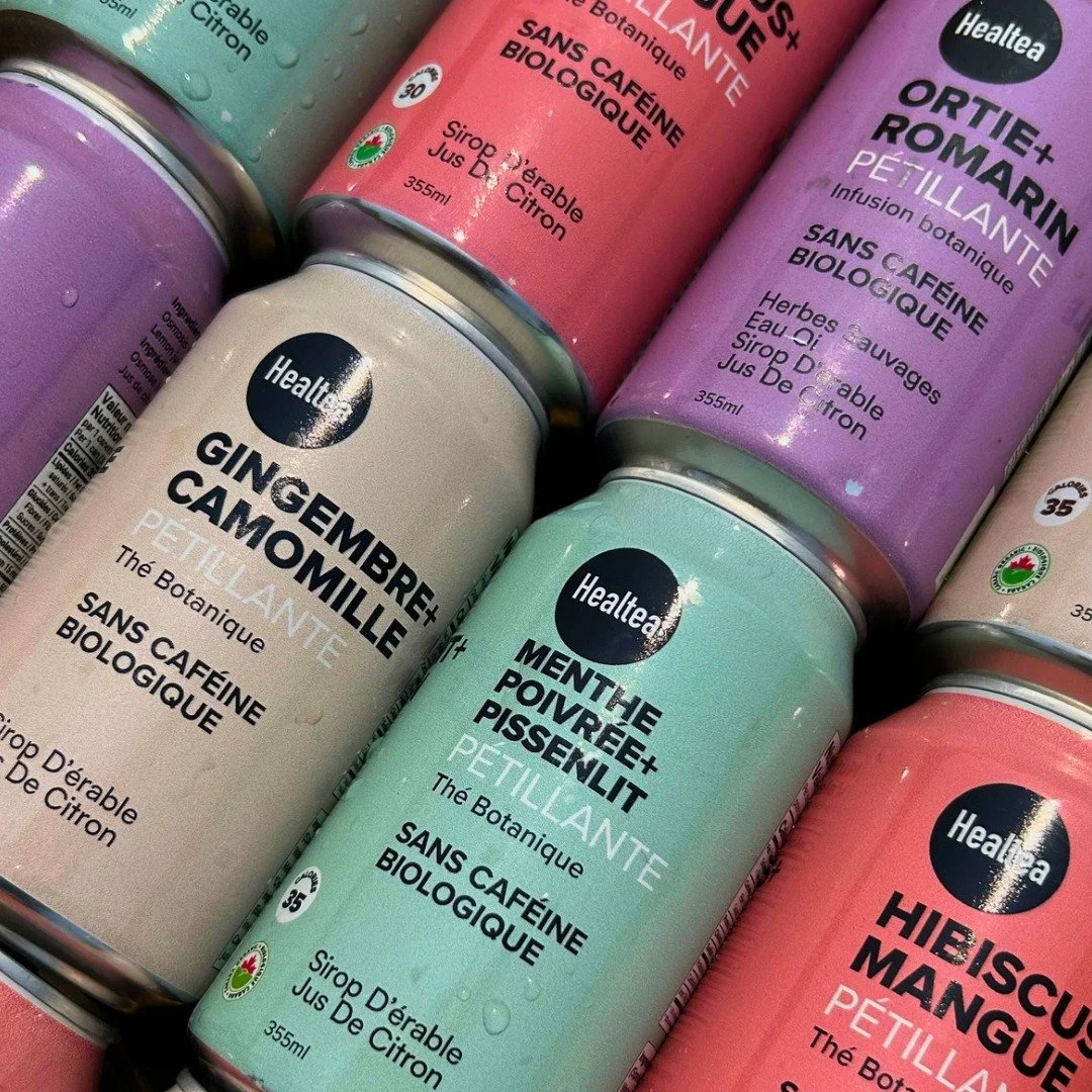 Assorted cans of herbal infusions with colorful packaging, labeled with flavors like ginger, lemon, mint, and hibiscus, from a brand called Healtea.