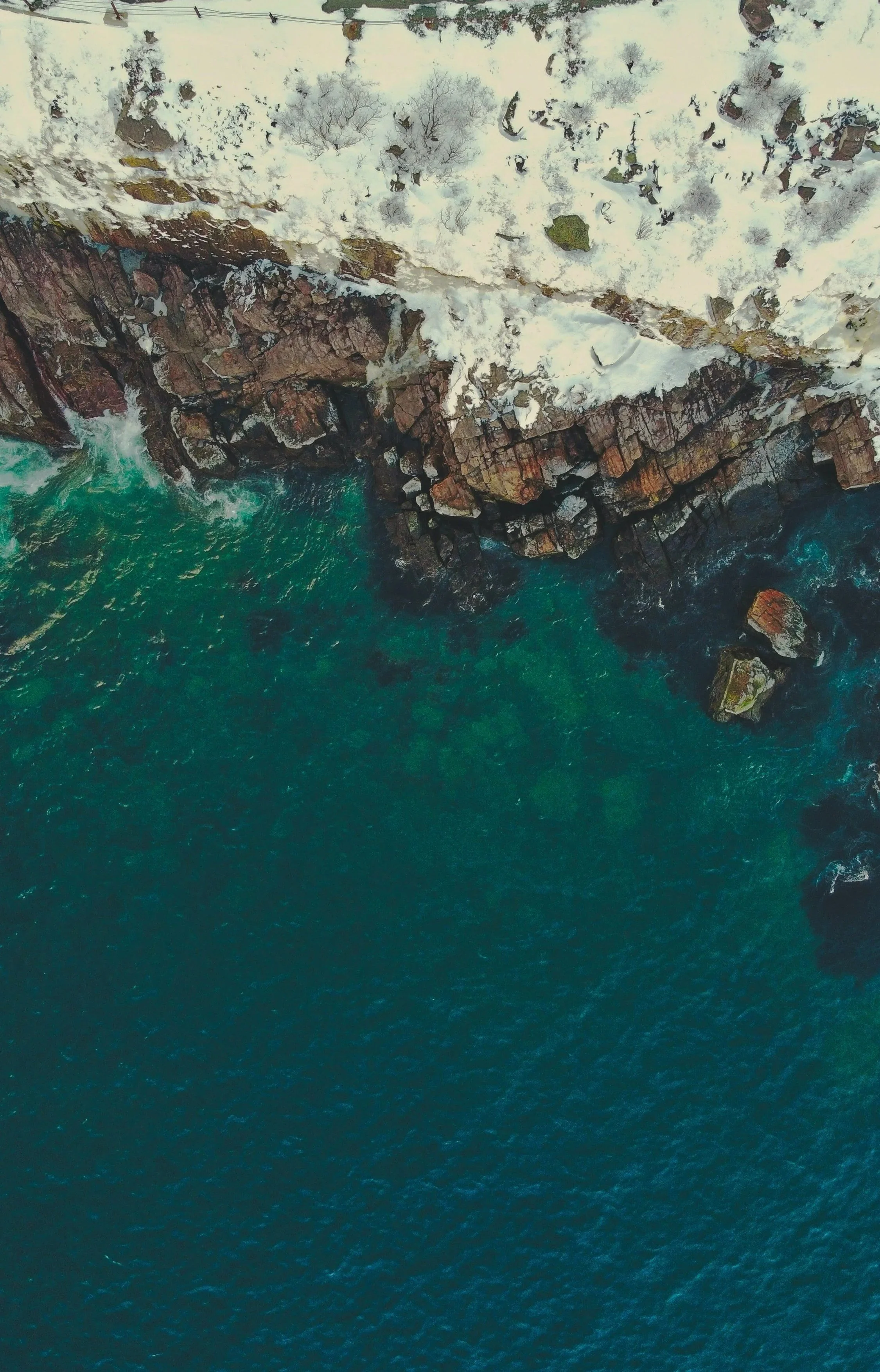 Calm, deep green ocean waters splashing against a rocky cliff.