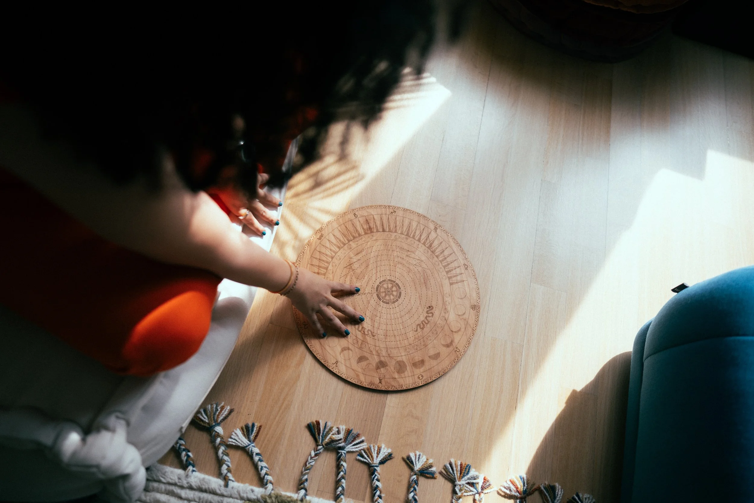 Person with blue nails laying hands flat on a circular wooden tuning chart on the floor.