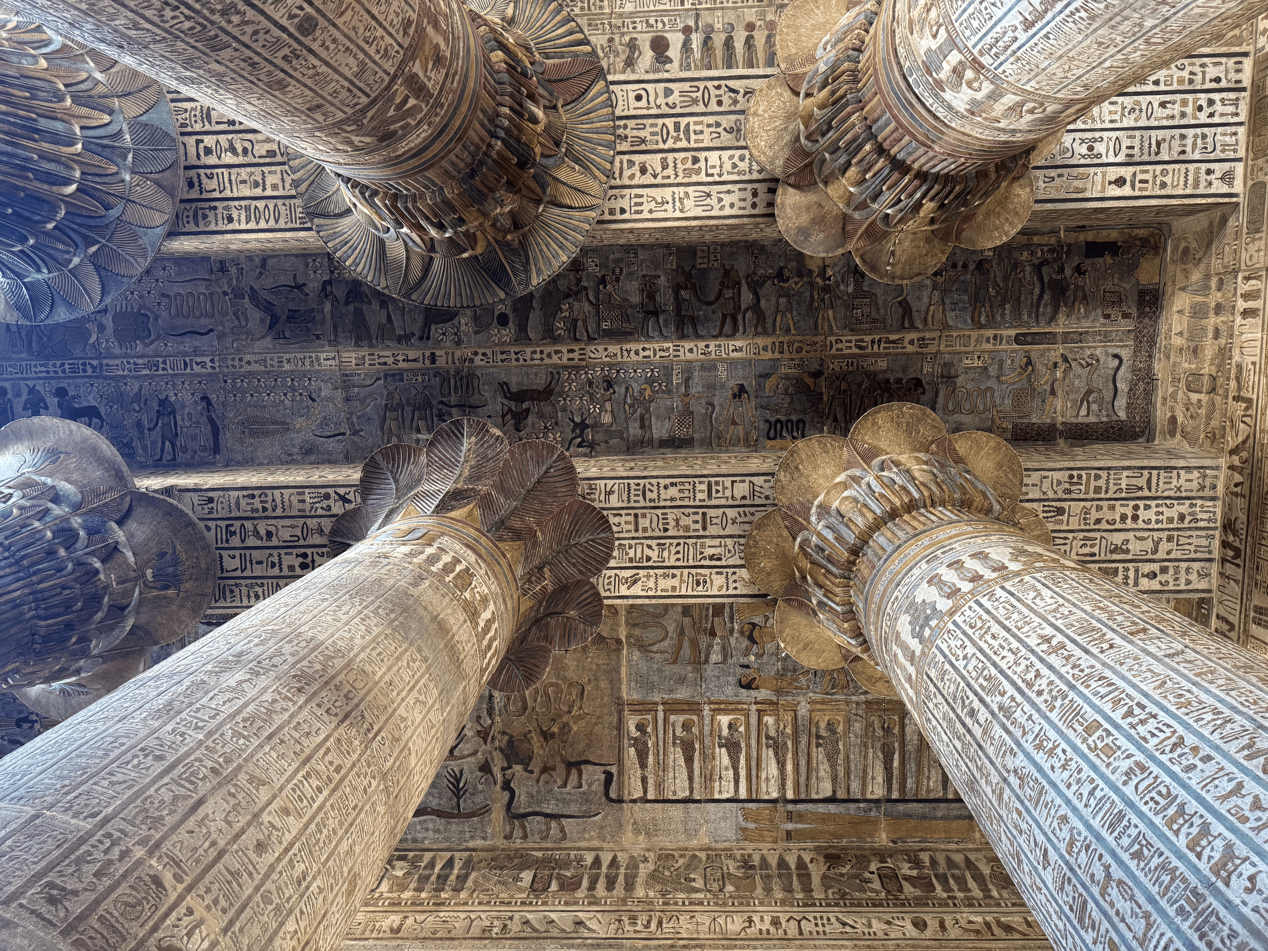 View of ancient Egyptian columns with hieroglyphic inscriptions on the walls and painted carvings depicting gods and figures.