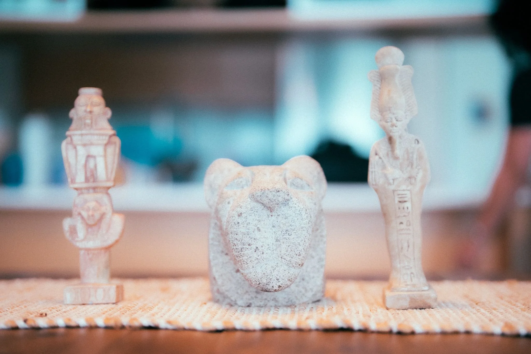 Collection of small ancient figurines and artifacts on display, including human and animal figurines, with a focus on a central figurine resembling a bear or feline made of a stone-like material, in a museum setting.