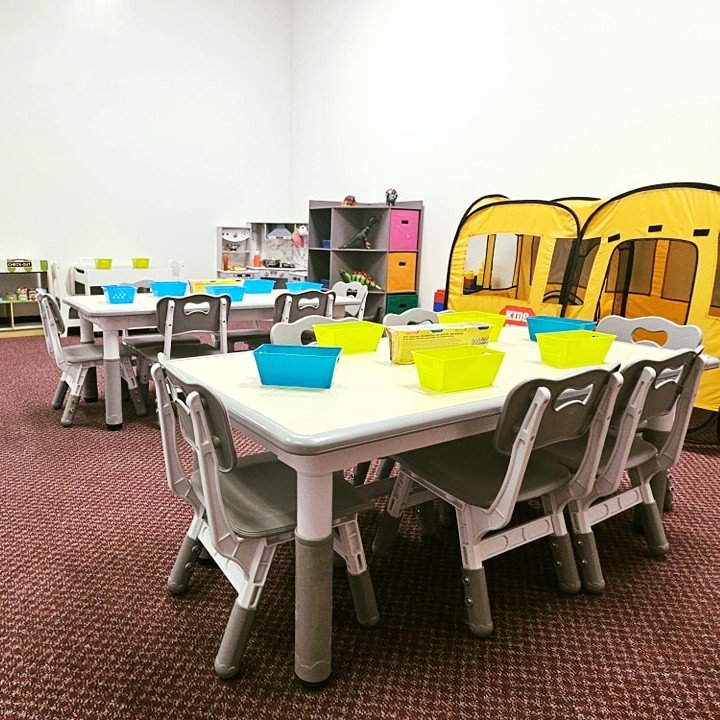 Children's playroom with toddler tables and chairs, colorful bins, and a yellow play tent.