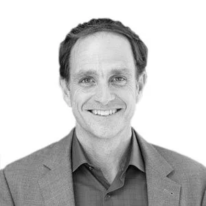 Black and white photo of a smiling man wearing a suit jacket and collared shirt