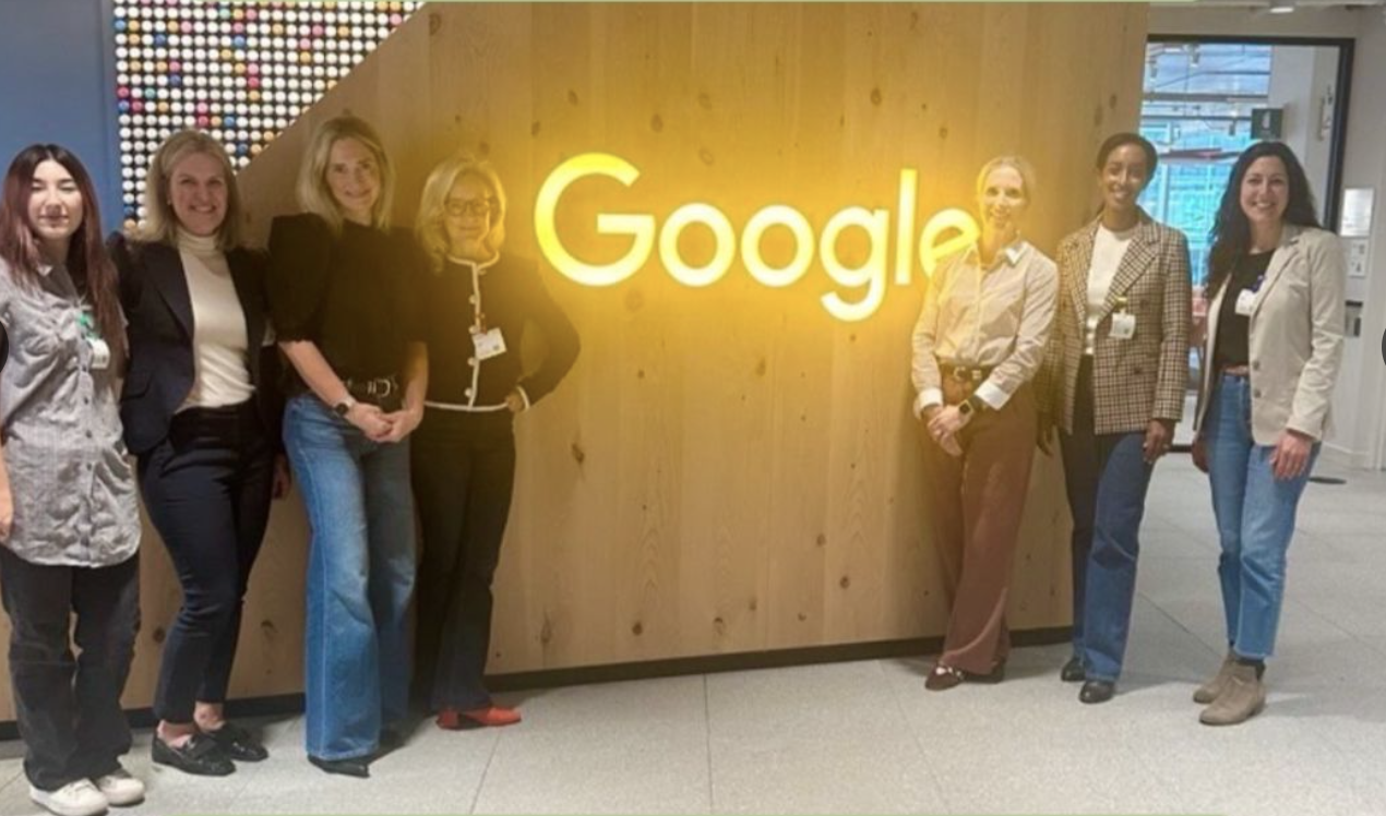 Group of women standing in front of a Google sign inside an office building.