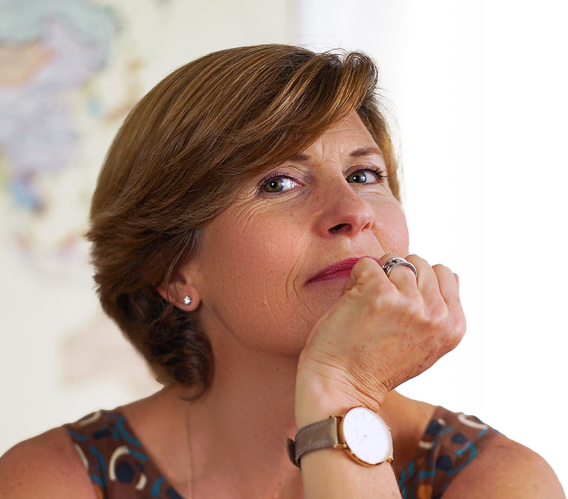 A thoughtful middle-aged woman with short brown hair and wearing a patterned sleeveless top, a watch, and a ring, resting her chin on her hand with a contemplative expression.