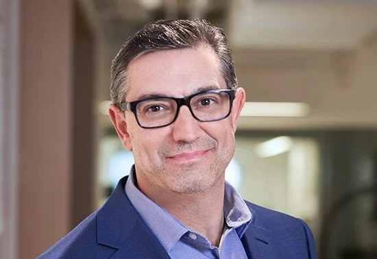 Professional man in a blue suit and glasses smiling in an indoor setting.