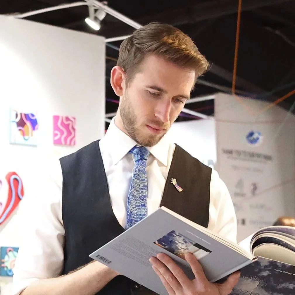 A man in business attire, with a vest and tie, browsing through a book or magazine at an indoor event or exhibition.