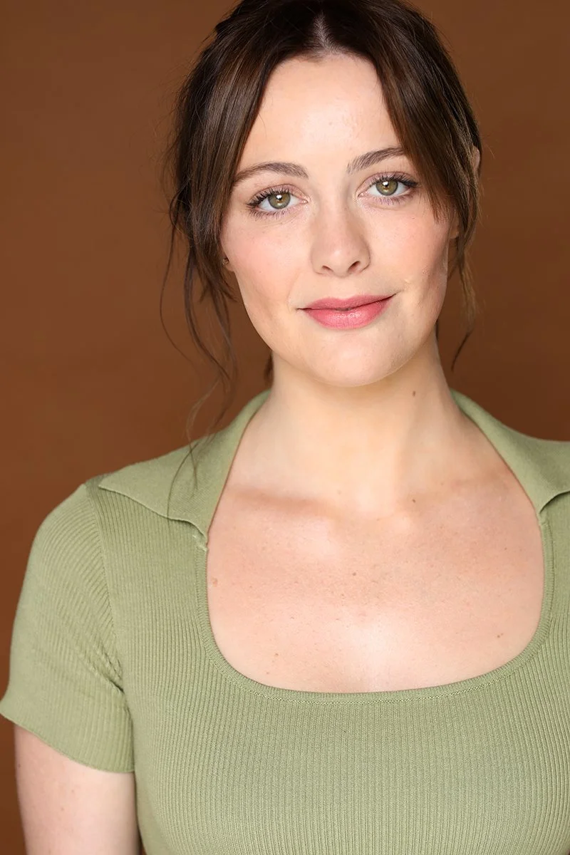 A young woman with brown hair and green eyes, smiling softly, wearing a light green top against a brown background.