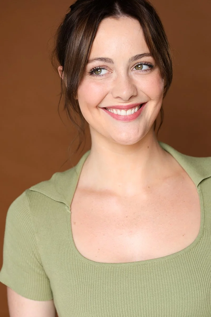 Close-up of a smiling woman with brown hair and light makeup, wearing a light green shirt, against a brown background.