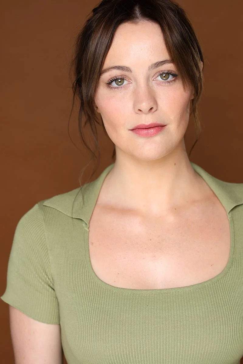 Portrait of a woman with shoulder-length brown hair, wearing a light green top, and standing against a brown background.