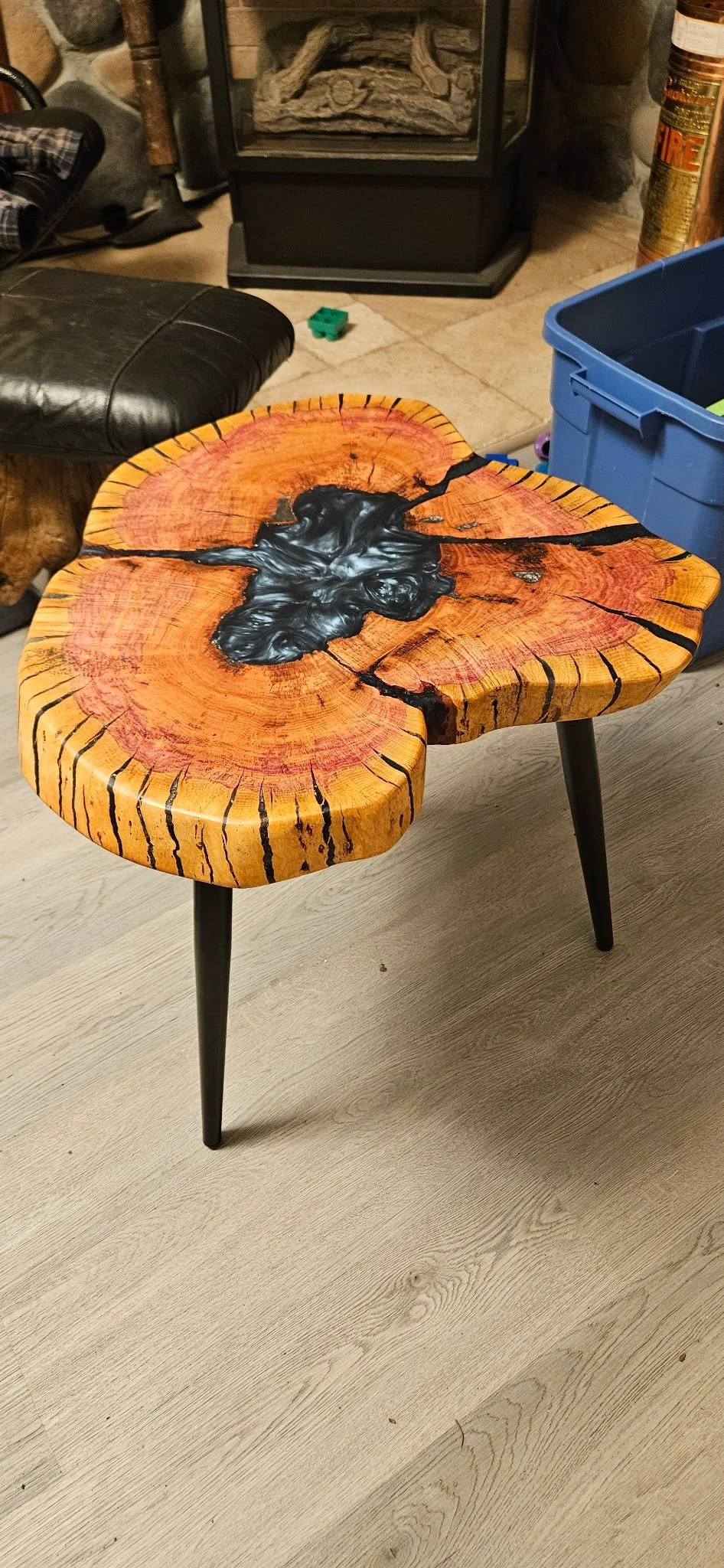 A wooden table with a natural, irregular shape, featuring a black resin river flowing through the center, emphasizing the wood grain and cracks.