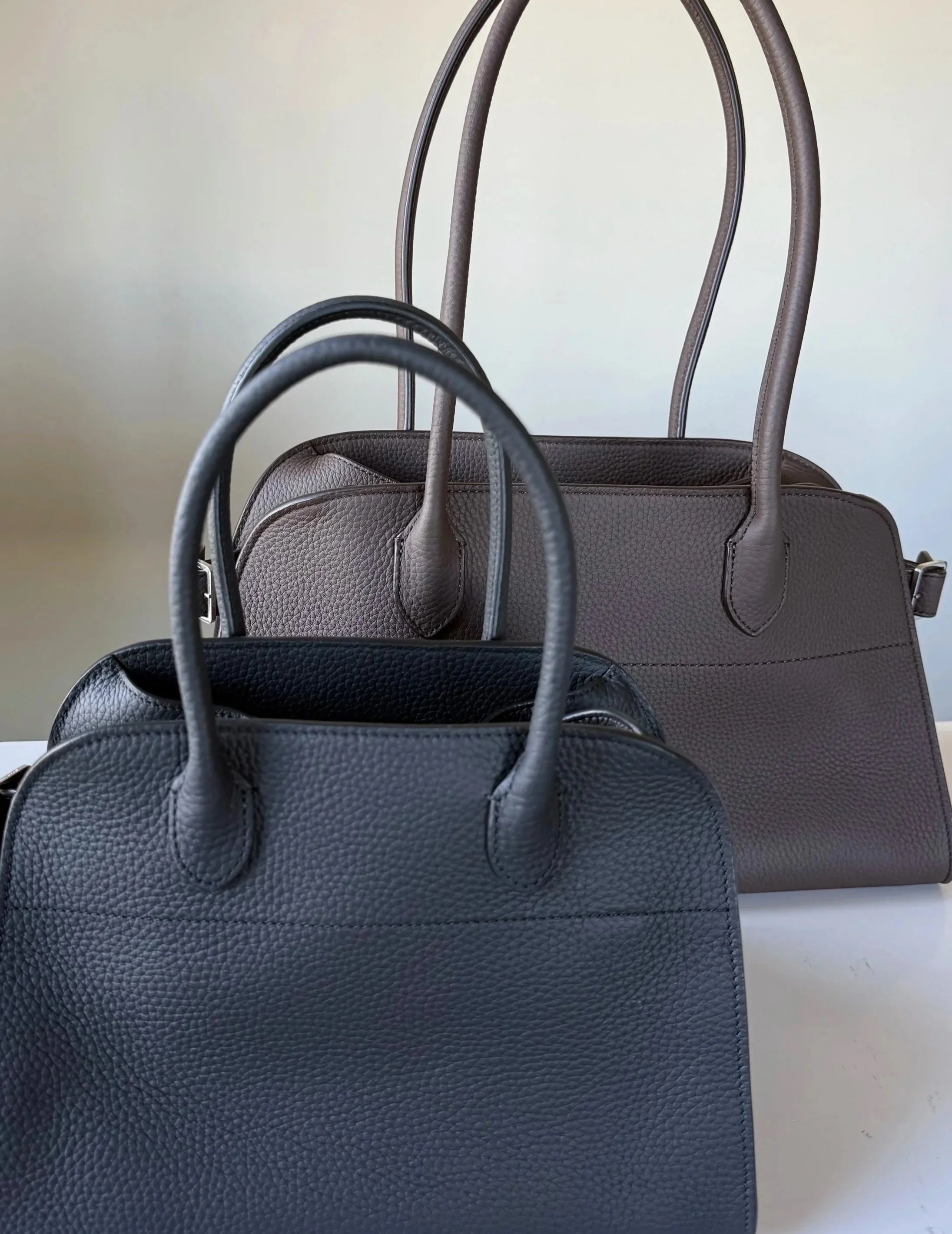 The Row Margaux 10 in black matte grained calfskin and Margaux Shoulder 12 in deep brown matte grained calfskin side by side — comparing sizes for Violetta’s Bags review.