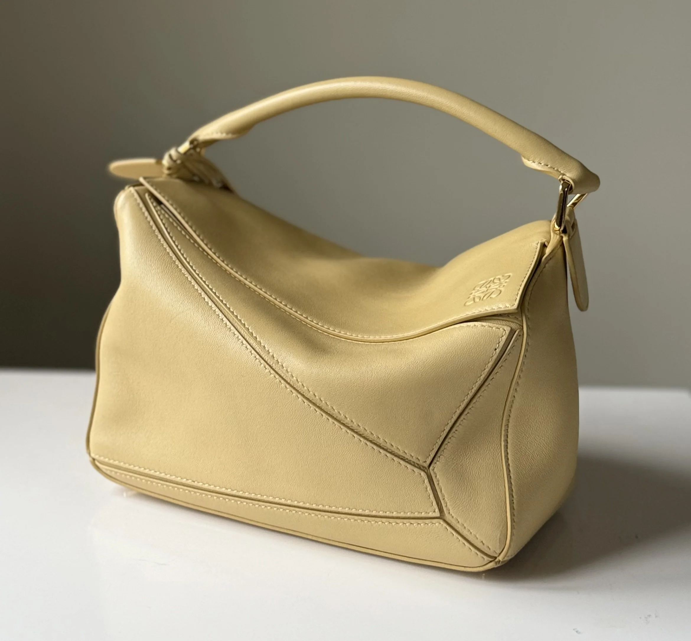 Loewe Small Featherlight Puzzle bag in Dark Butter leather displayed on a table — featured on Violetta’s Bags for its lightweight design and elegant craftsmanship.