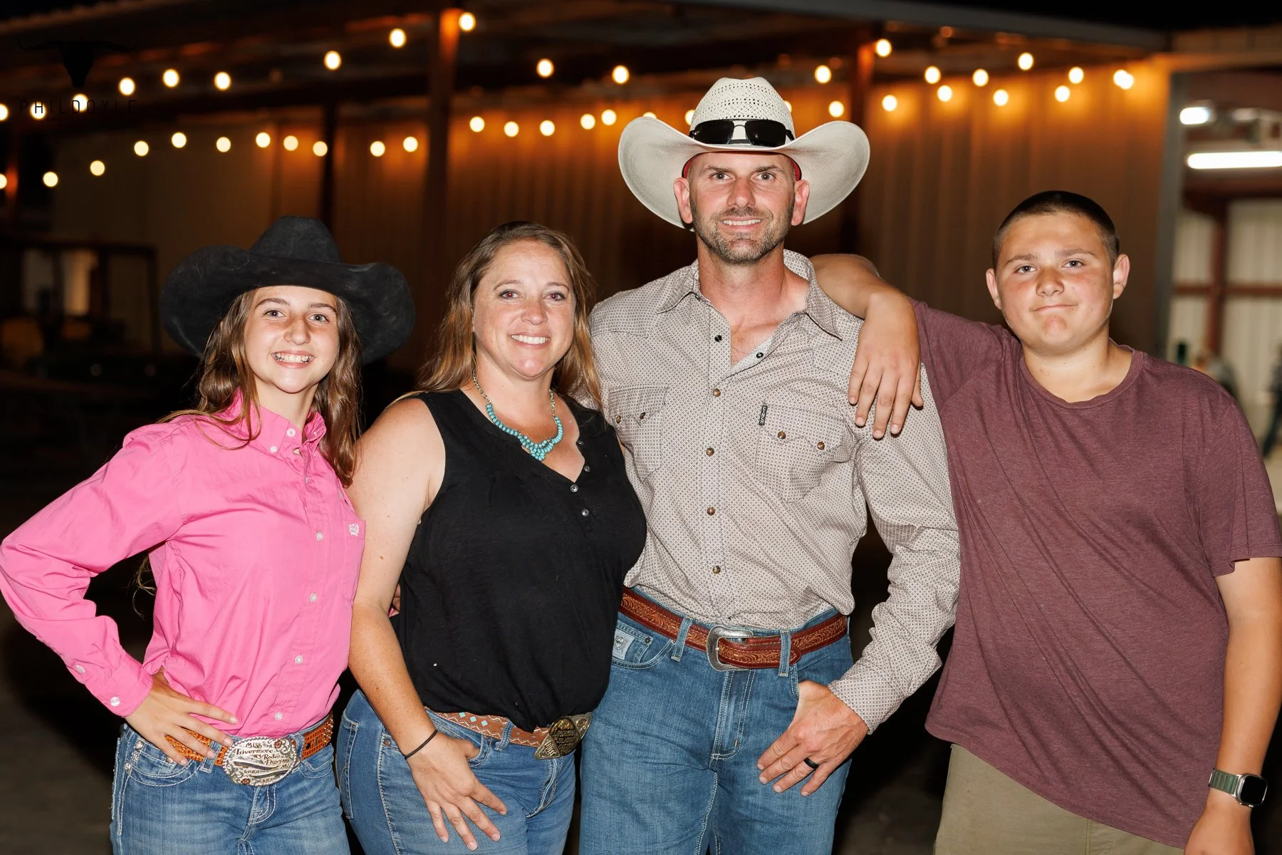 Family gathered at a rustic indoor venue, dressed in western attire, with string lights overhead.
