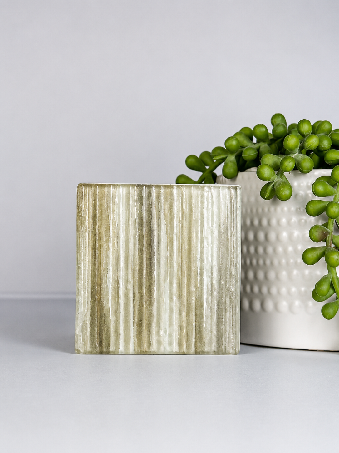 Decorative marble square pot and a textured white planter with green succulent plant on a plain surface.