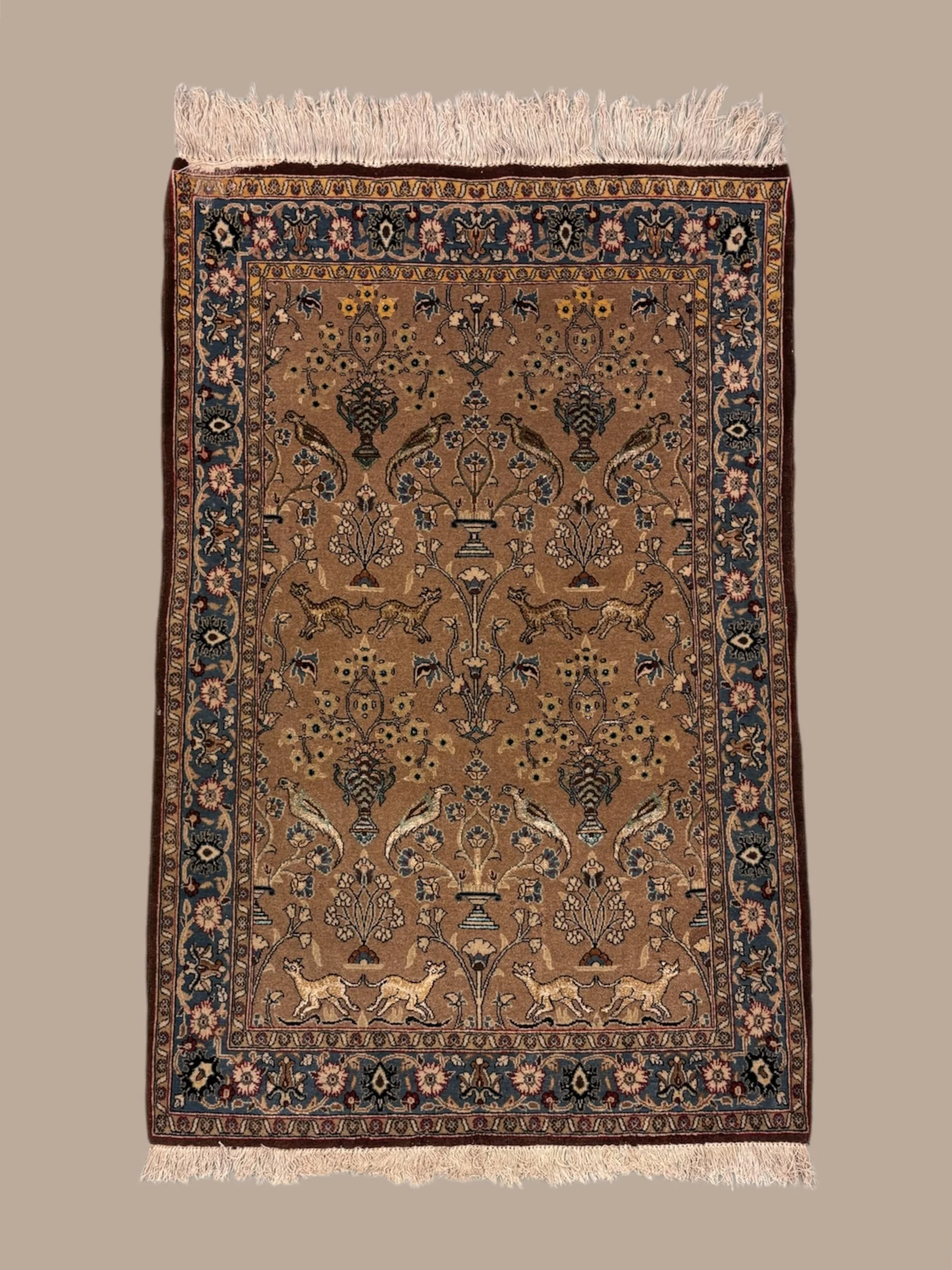 An ornate Persian-style rug with floral and animal motifs in earthy tones, bordered with intricate patterns and fringes at the ends.