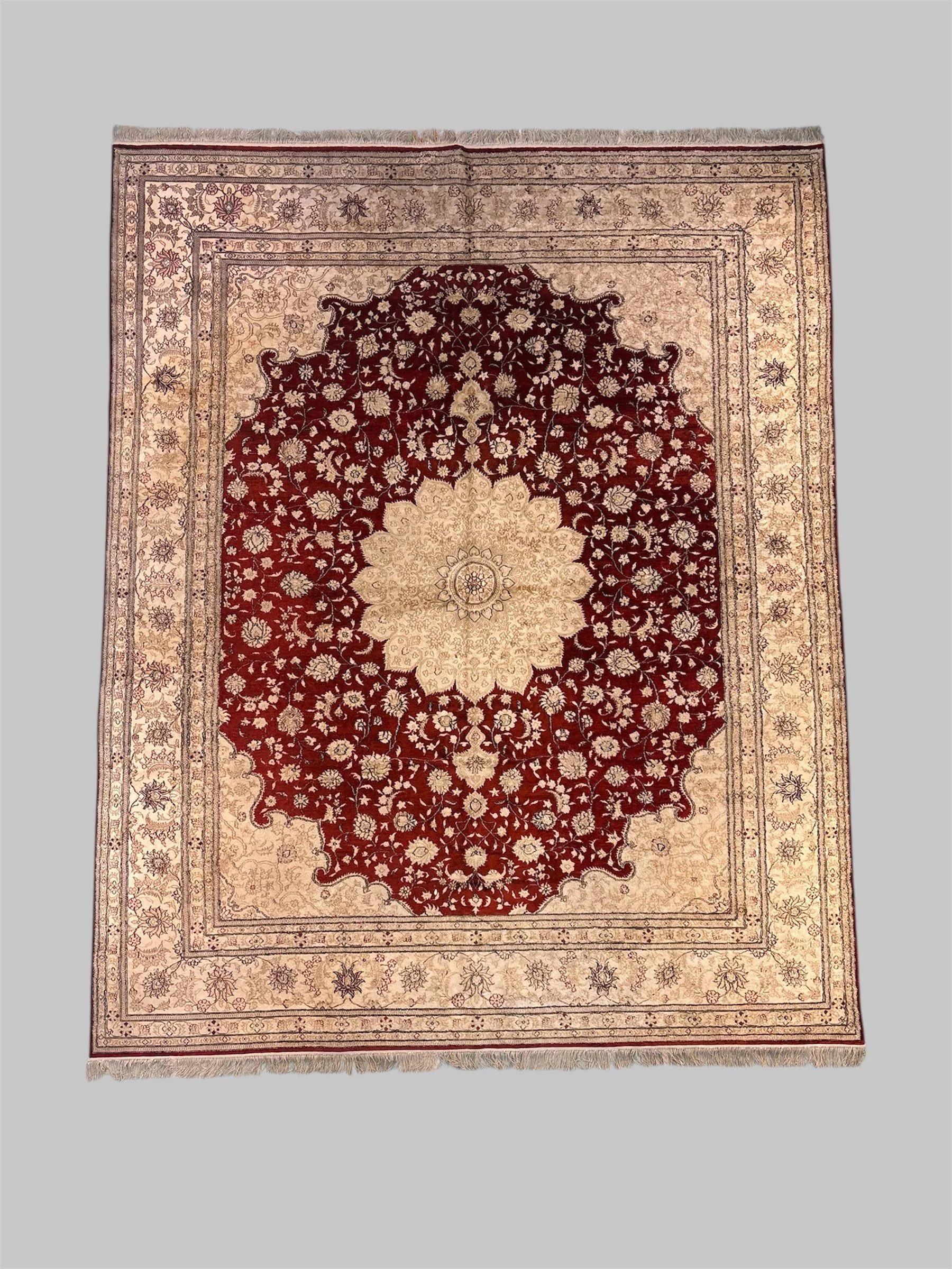 A traditional patterned area rug with a central floral medallion design in shades of beige, red, and black, featuring intricate floral and geometric borders.