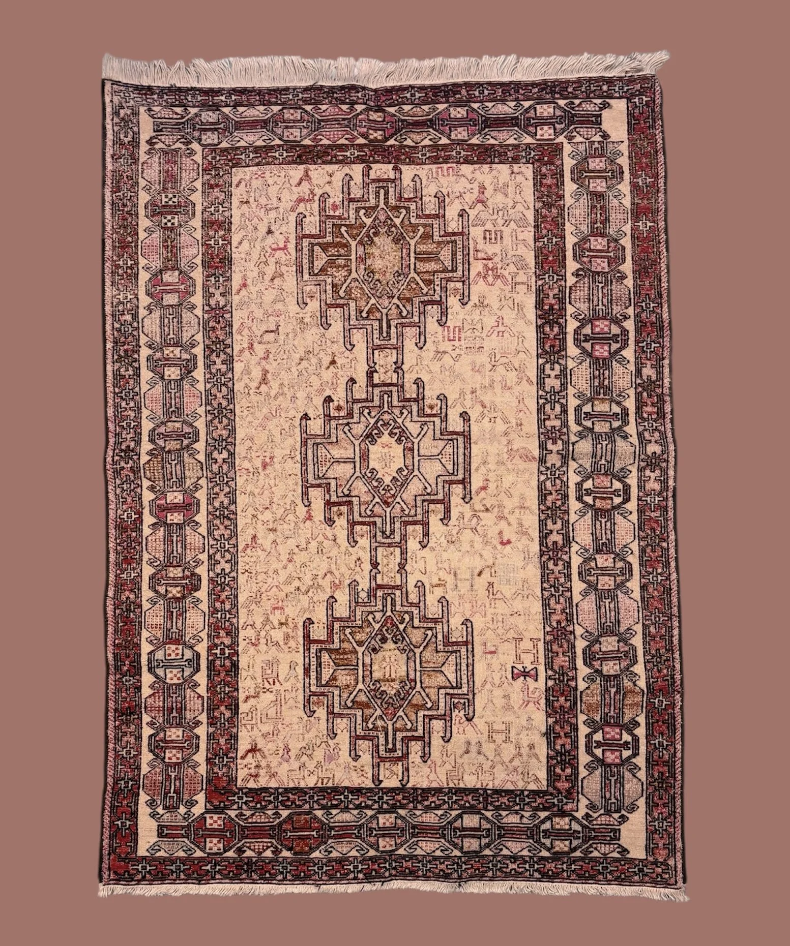 An ornate traditional rug with geometric patterns in red, black, and beige, featuring a central medallion and intricate borders, laid on a brown background.