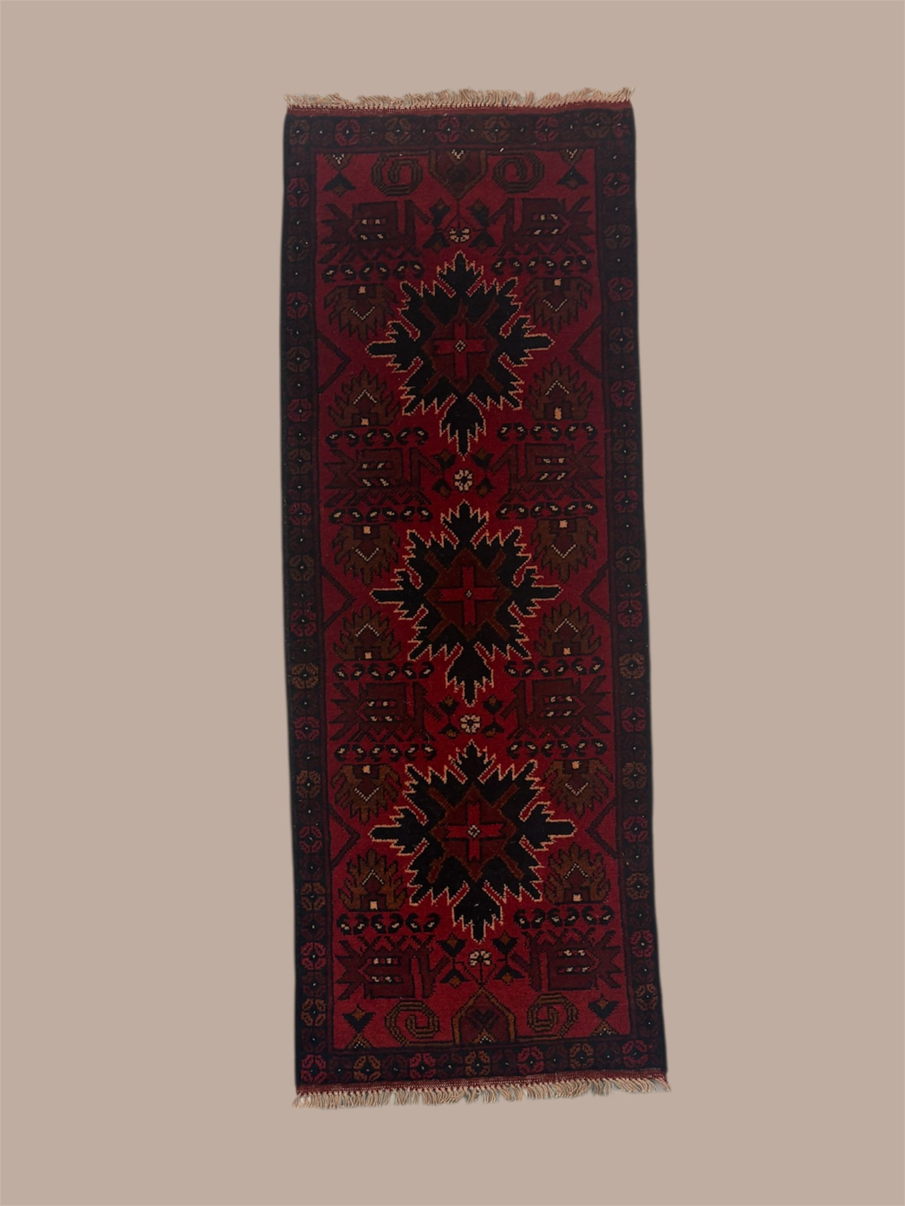A narrow traditional Persian-style rug with a central black and red floral pattern, surrounded by geometric designs in deep red, black, and brown, with fringes on both ends.
