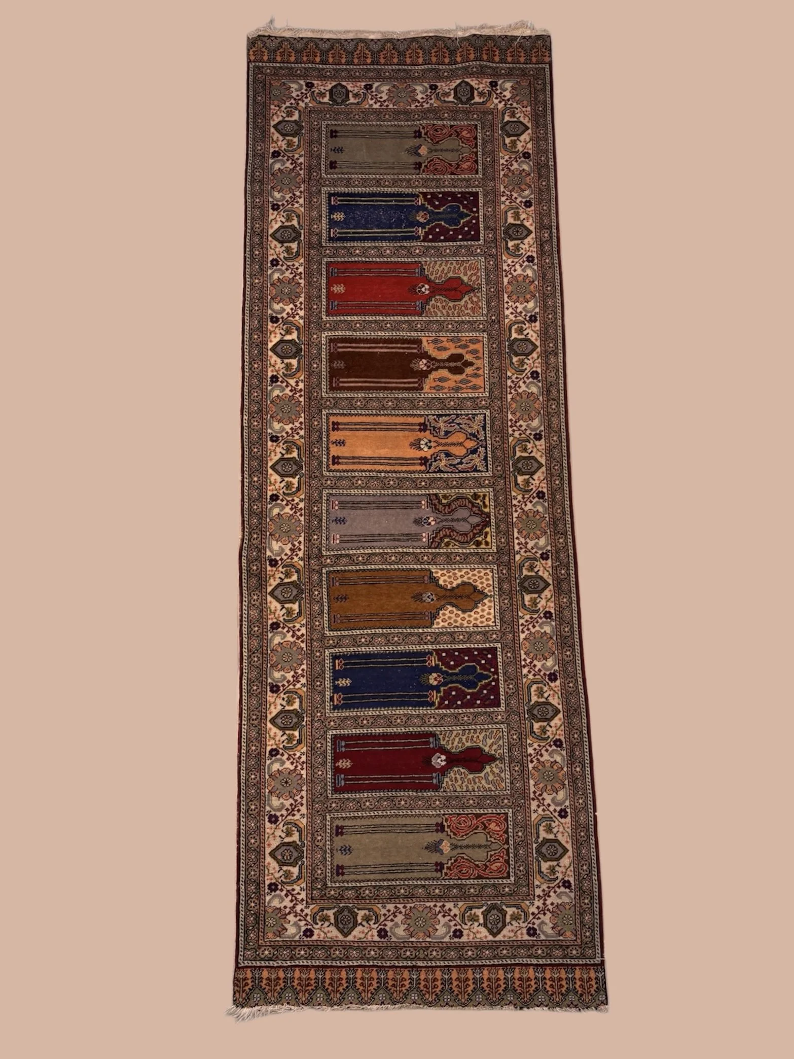A long, rectangular, ornate rug with intricate floral patterns and geometric borders in various earthy tones including red, blue, beige, and brown.
