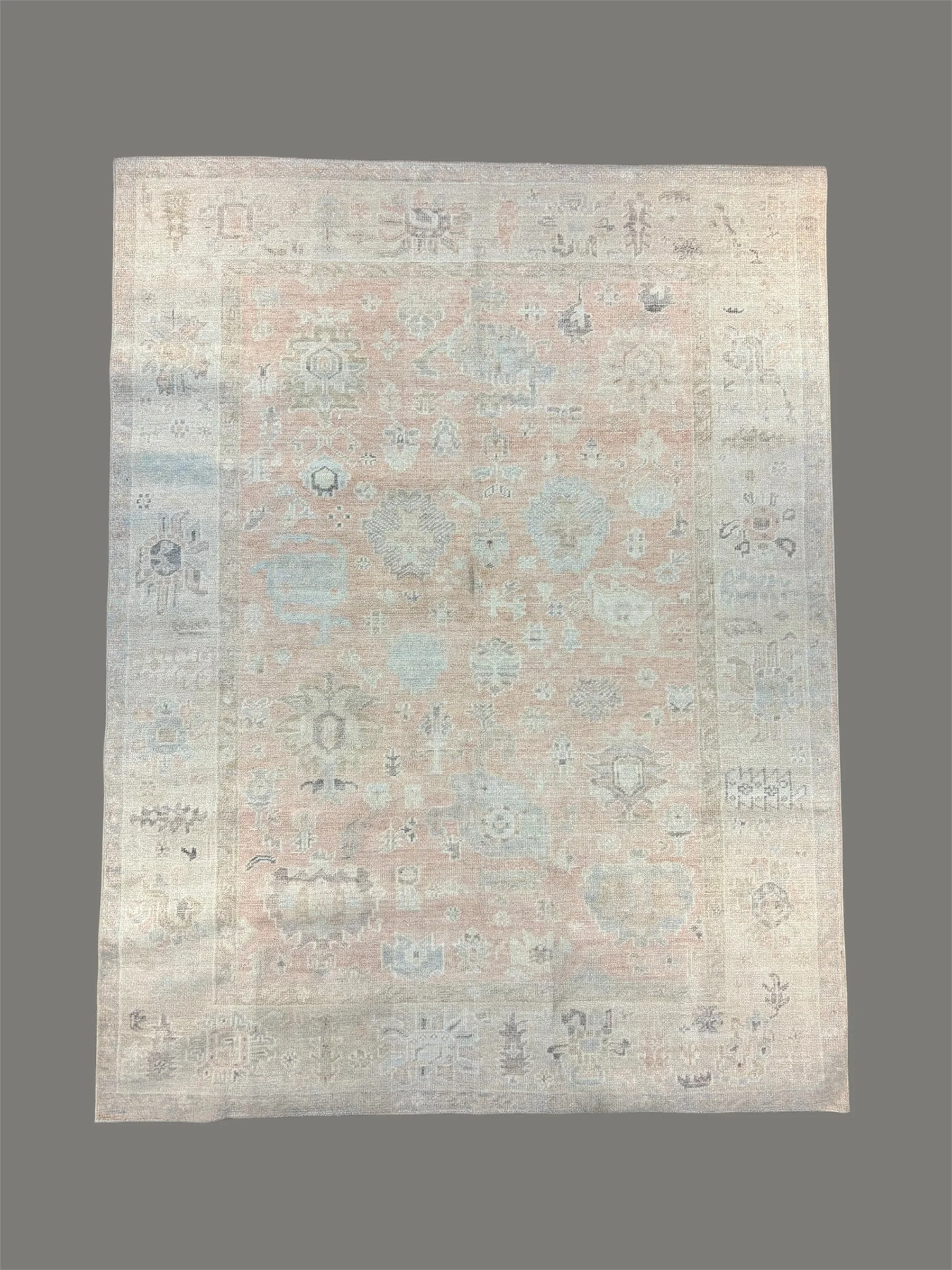 A faded, antique, rectangular oriental rug with intricate geometric and floral patterns in pastel shades of pink, blue, and beige.