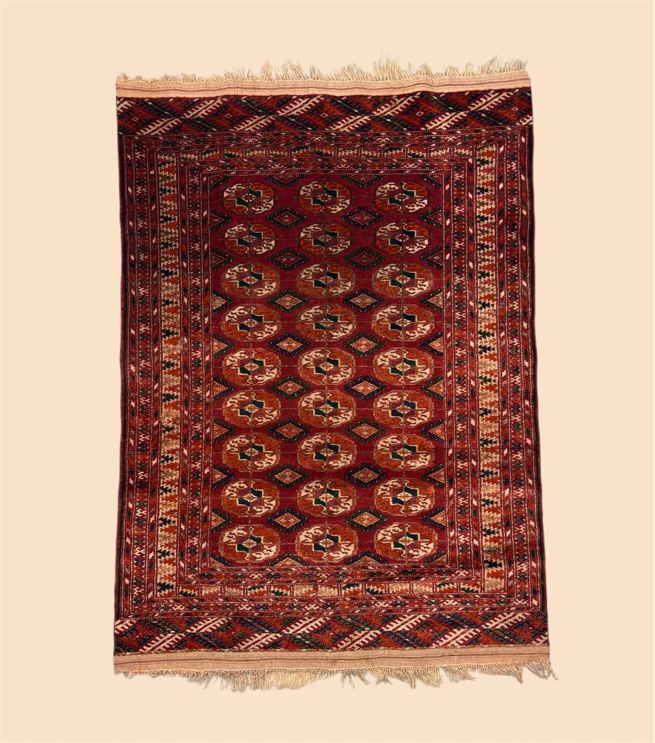 A traditional Persian-style rug with a dark red background and intricate geometric patterns in orange, green, black, and cream. The rug has a border with repeating geometric designs and fringes at the top and bottom edges.