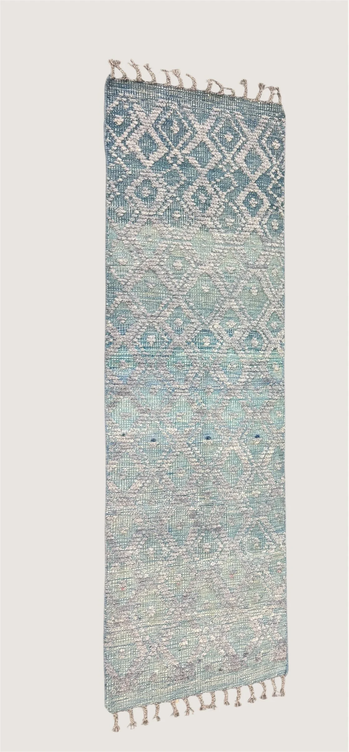 A long decorative woven rug with intricate geometric patterns in shades of blue and white, featuring fringes on both ends.