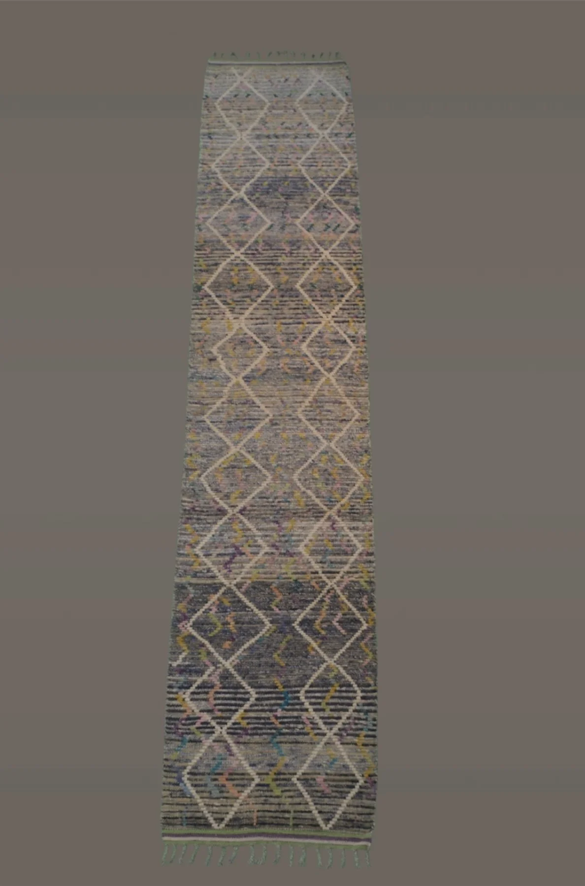 A long, narrow rug with an intricate geometric pattern of interconnected diamonds and zigzag lines, featuring multicolored details on a predominantly dark background, with fringes at the end.