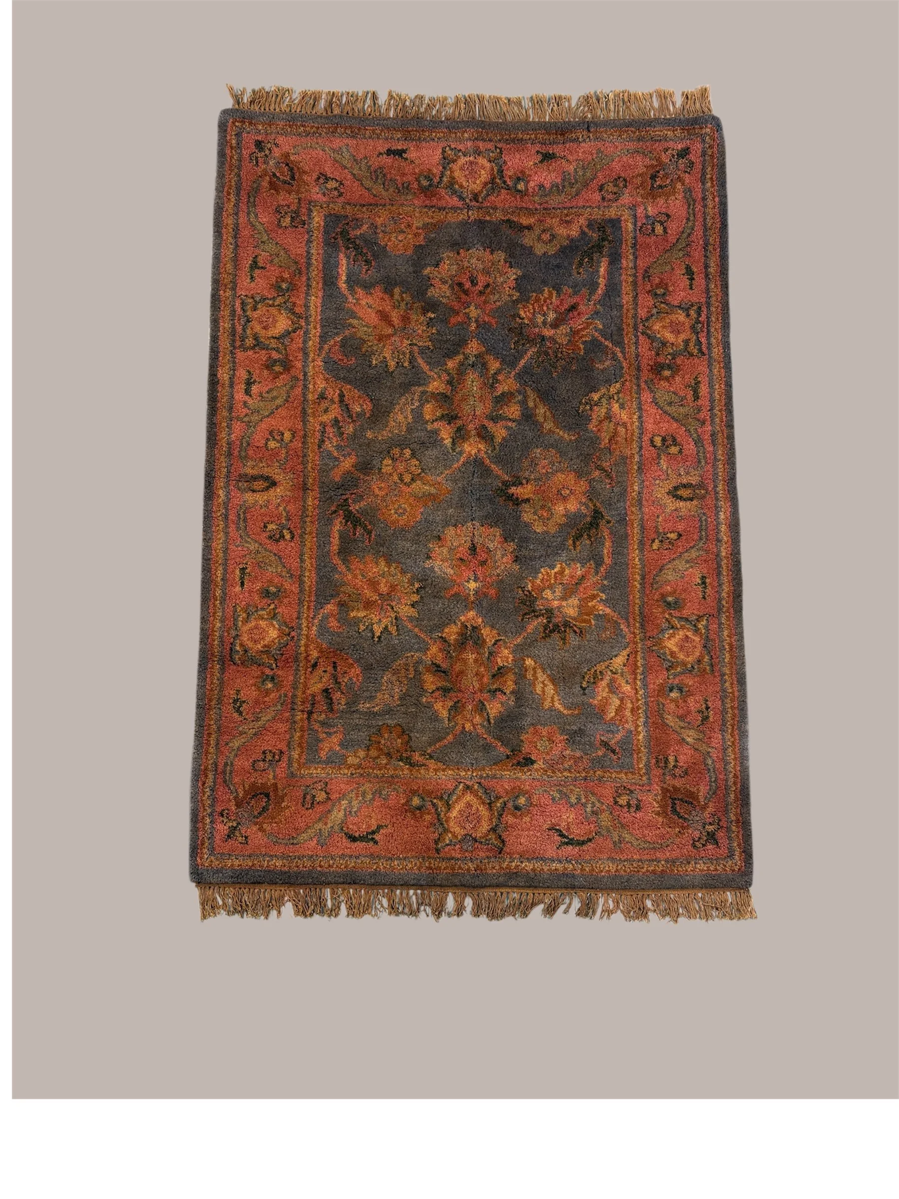 A vintage rectangularArea rug with fringed edges, featuring a central floral pattern in red, black, and yellow tones, set against a light neutral background.