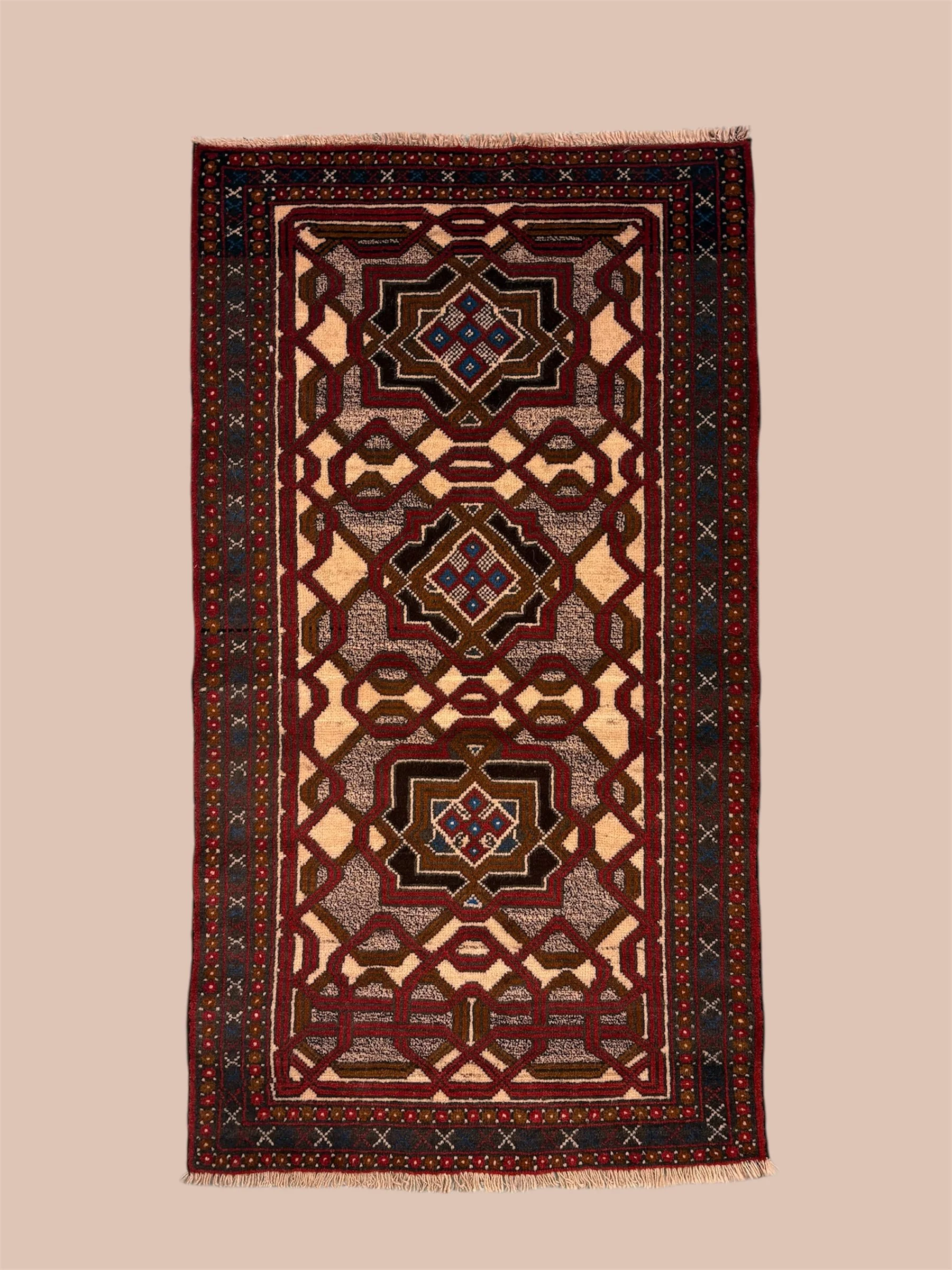A rectangular patterned rug with red, brown, black, cream, and blue geometric designs on a beige background.