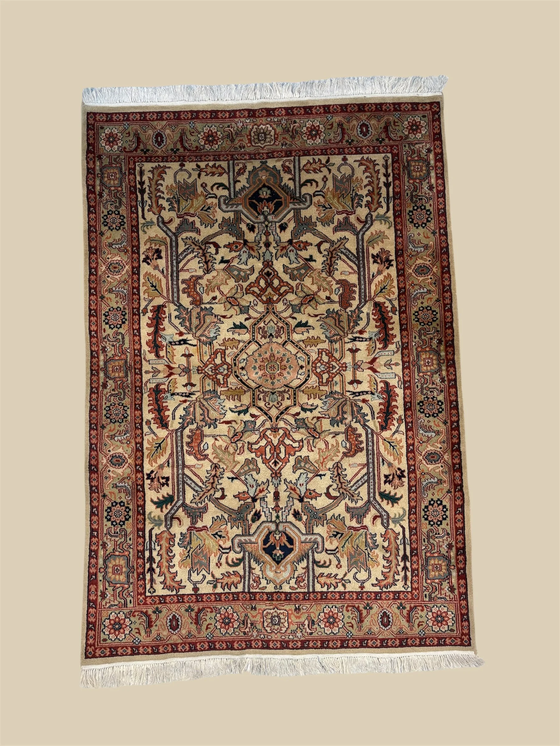 An ornate Persian-style rug with intricate floral and geometric patterns in red, cream, black, and beige colors, finished with white fringes at the top and bottom edges.