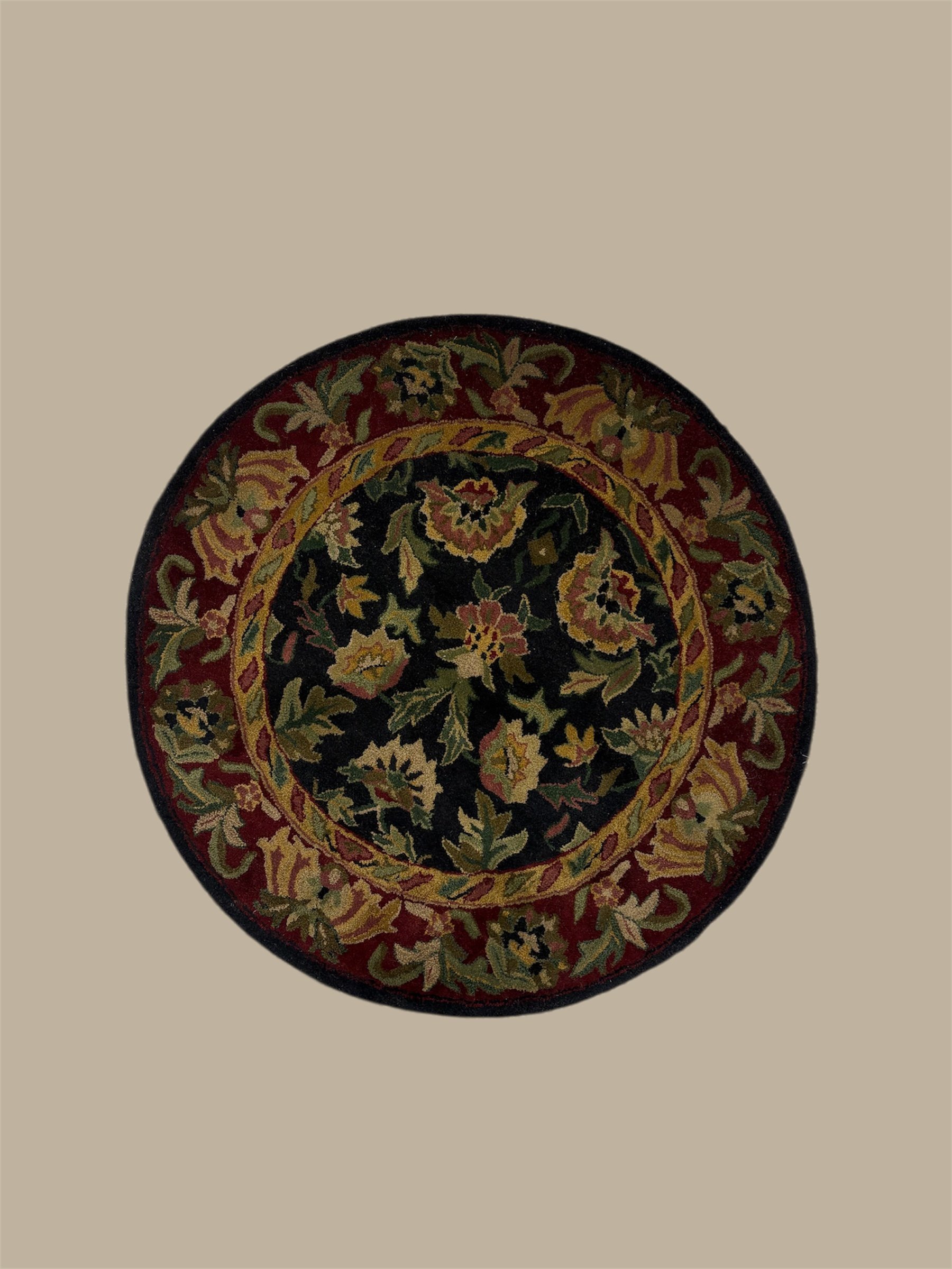 Top part of an ornate circular rug with floral patterns in black, red, yellow, and green on a light beige background.