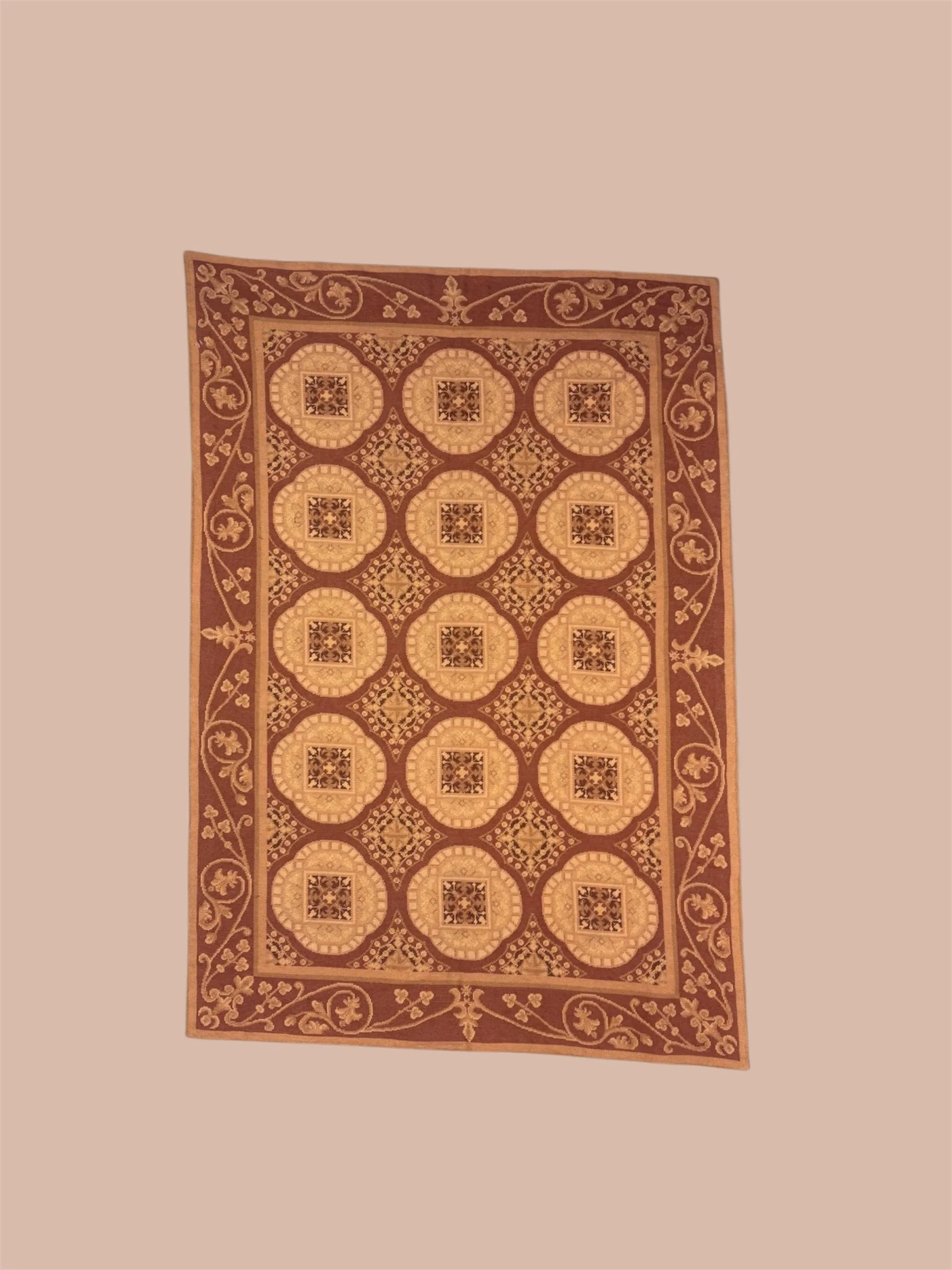 A rectangular decorative rug with intricate patterns in shades of brown and beige, featuring a floral border and geometric inner designs.
