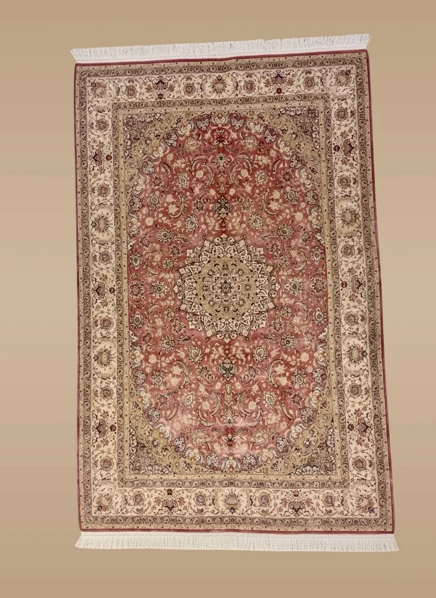 A traditional ornate Persian-style rug with intricate floral patterns in shades of red, beige, and cream, featuring a central medallion design and detailed border, lying on a plain beige floor.